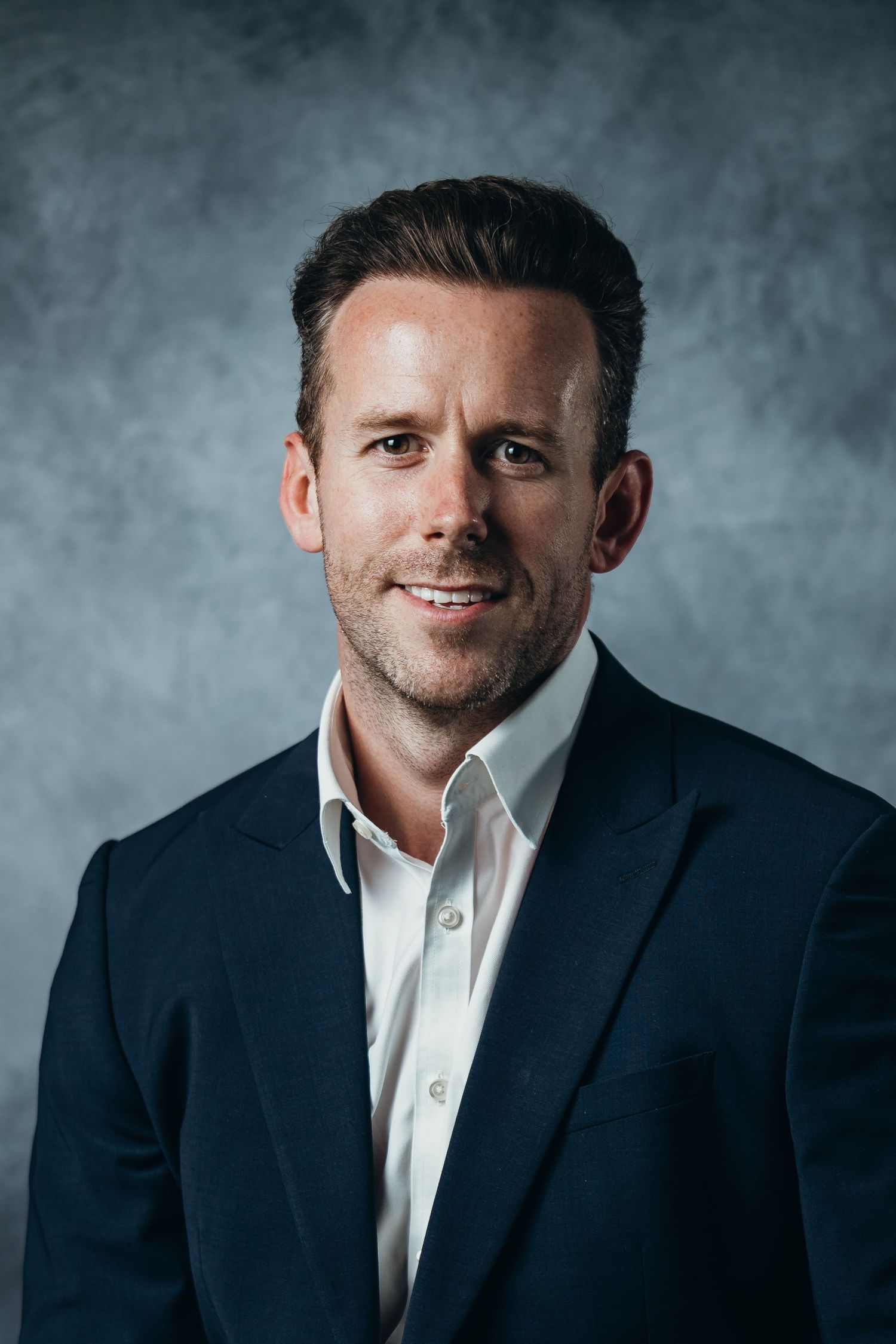 Professional headshot series showing different angles of a person in a navy suit and white shirt against a gray backdrop.