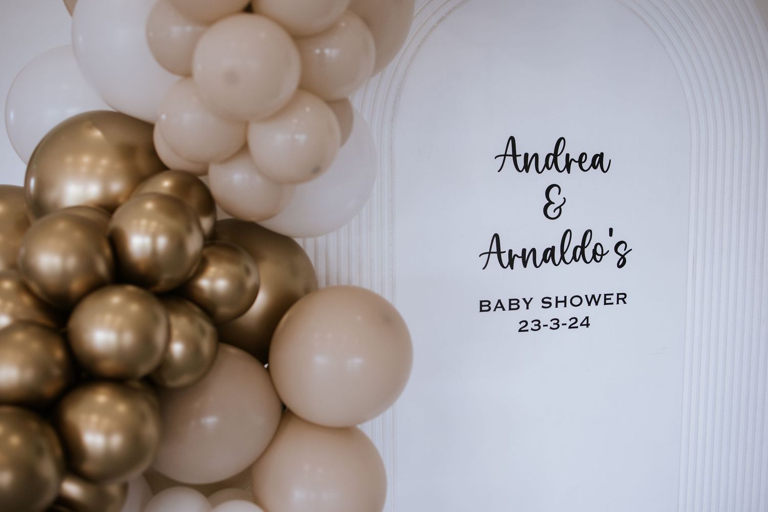 Elegant balloon arch with white and chrome gold balloons decorates a baby shower event.
