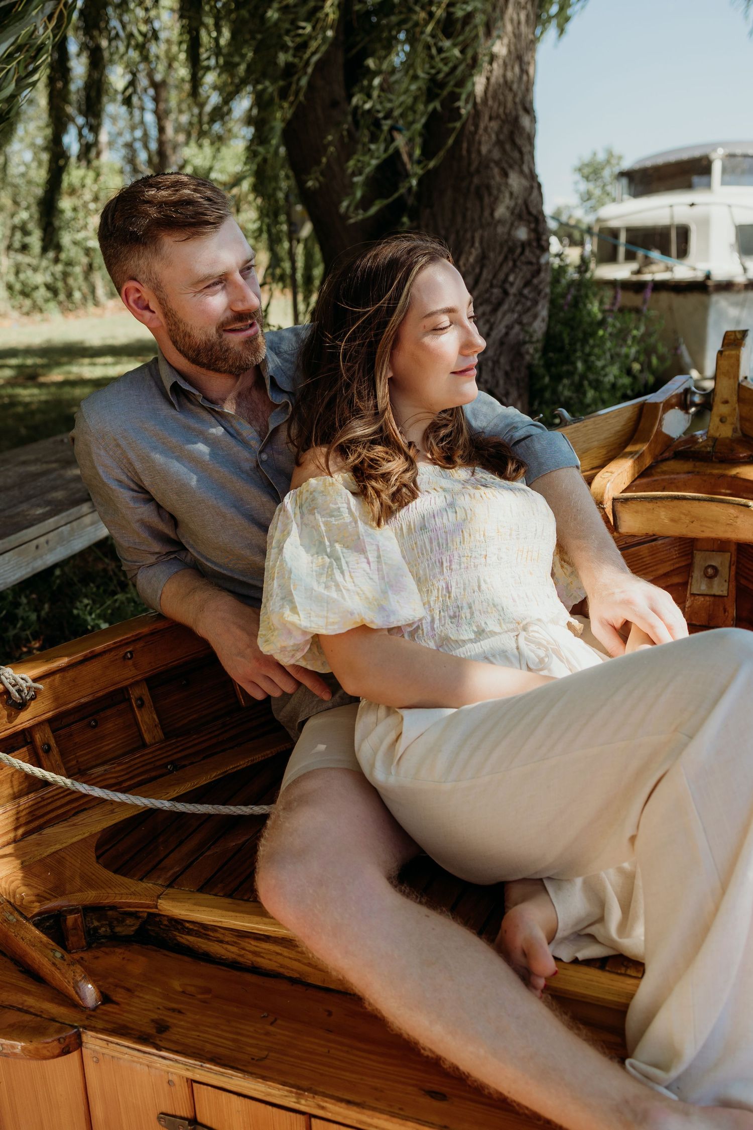 Romantic couple relaxing in wooden rowboat surrounded by willow trees.