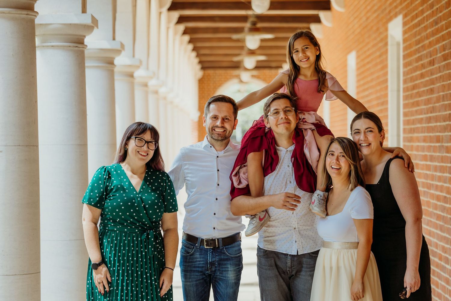 A group poses together under a columned brick portico with wooden beams.