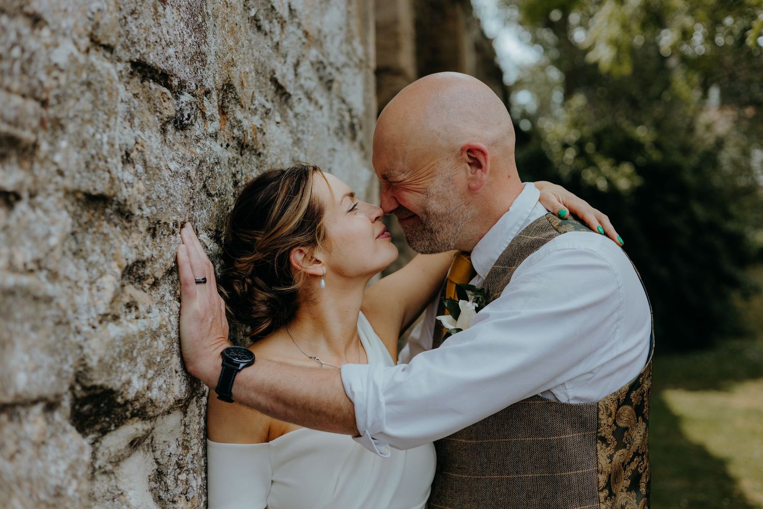 Romantic summer wedding portrait against weathered stone wall.