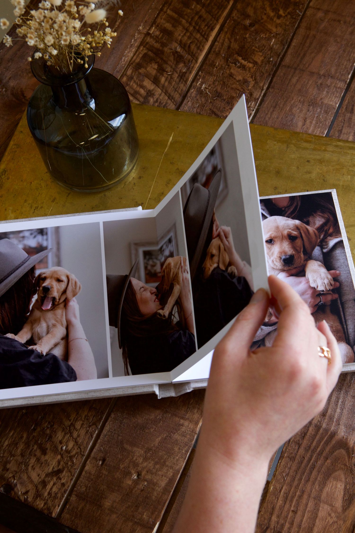 Hands flipping through a photo album showing dog pictures on wooden table.