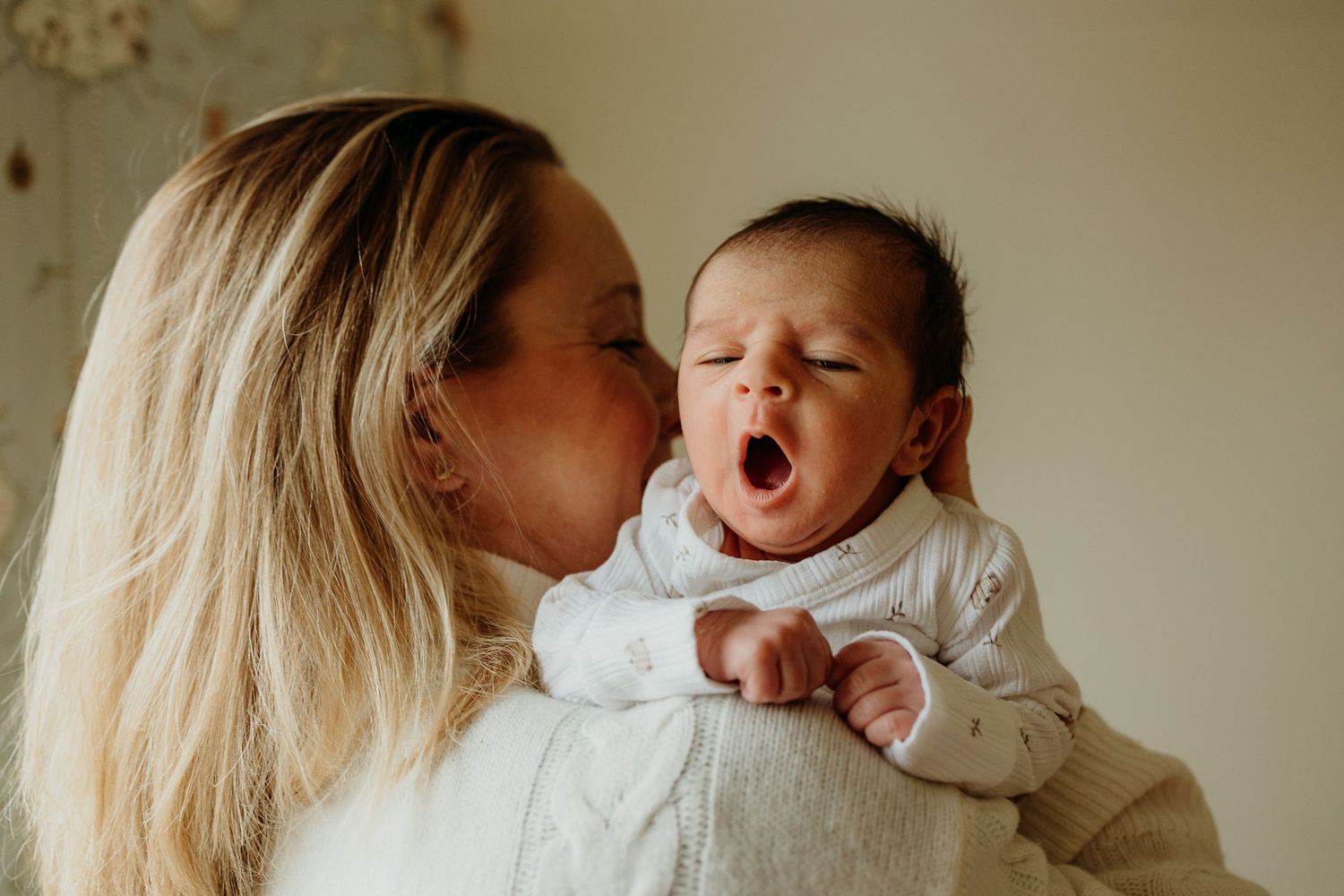Sweet interaction between parent and yawning baby in white clothing.