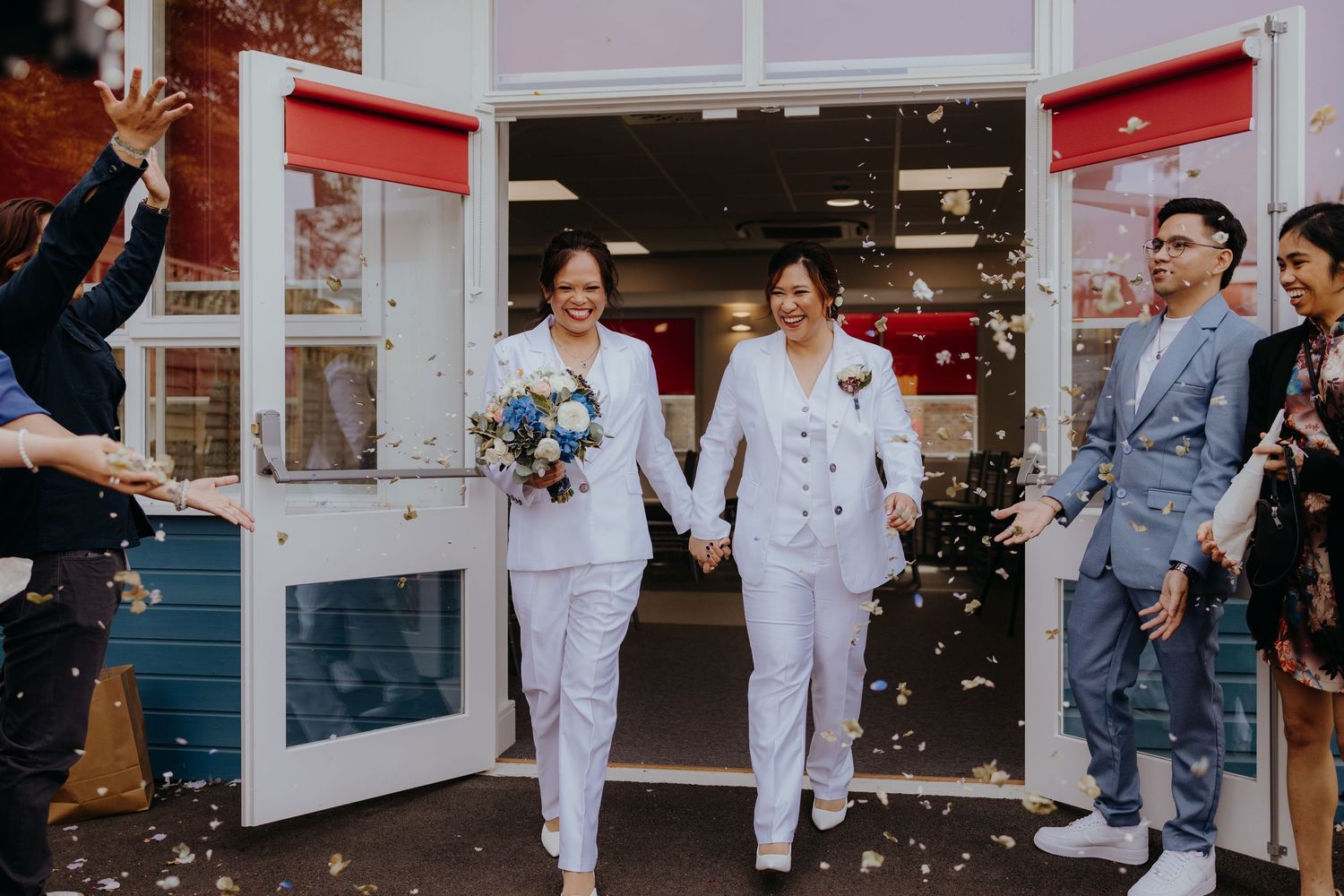 Wedding party celebrating with confetti outside building entrance.