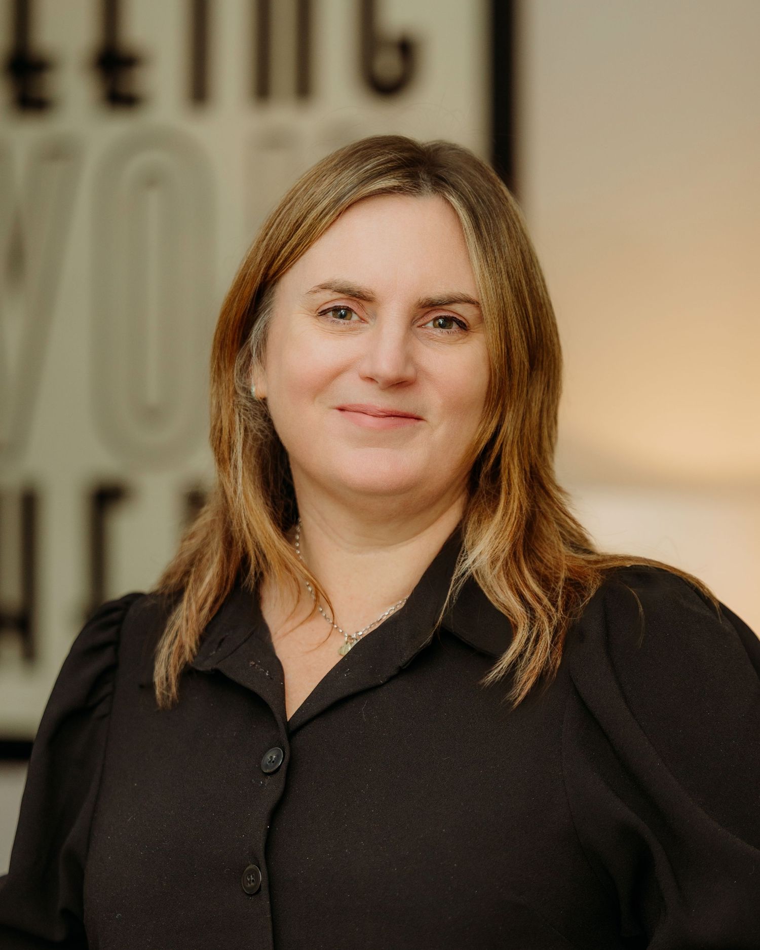 Professional portrait of someone wearing a black collared shirt against a beige background.