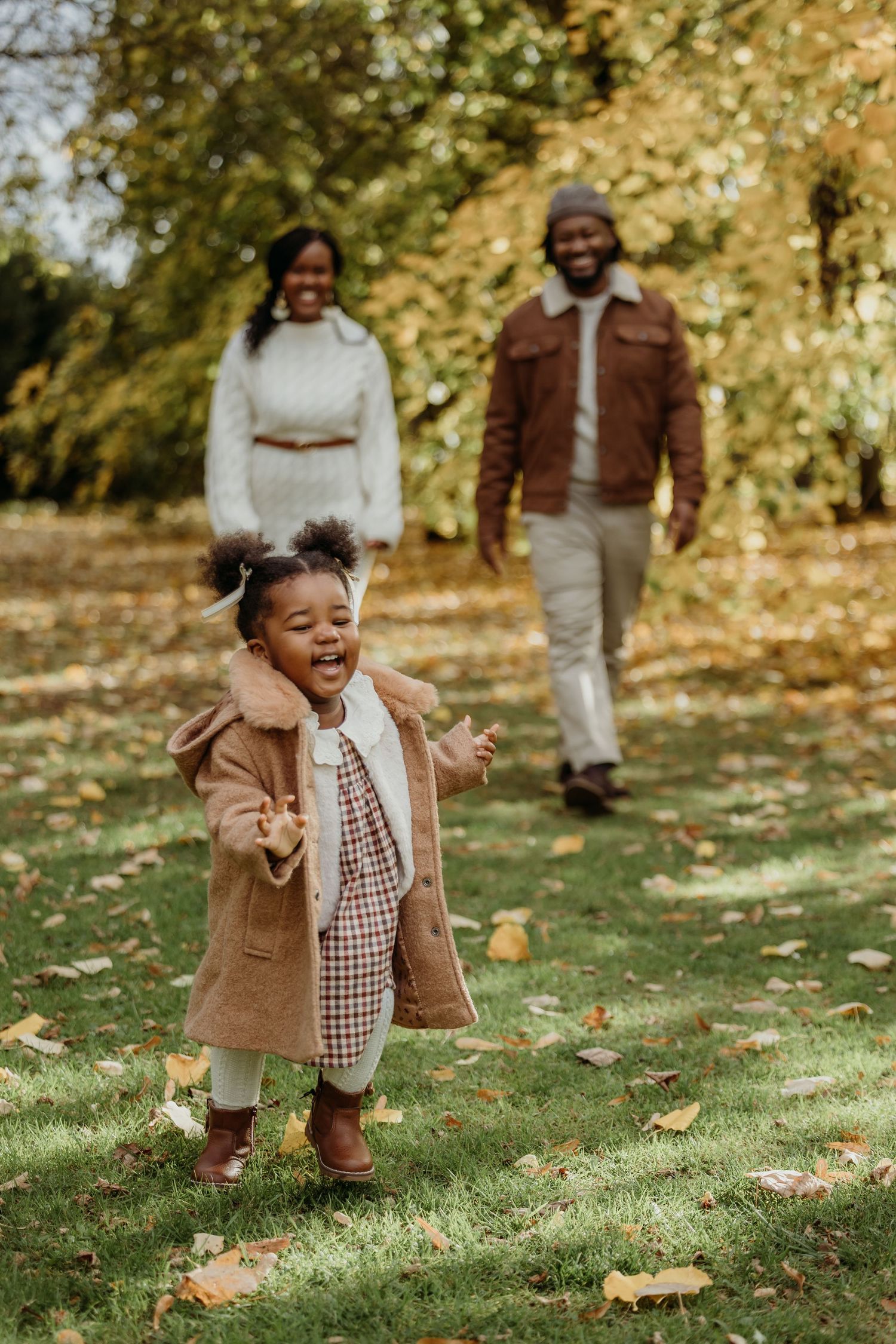 Child in brown coat playing joyfully among fallen autumn leaves.