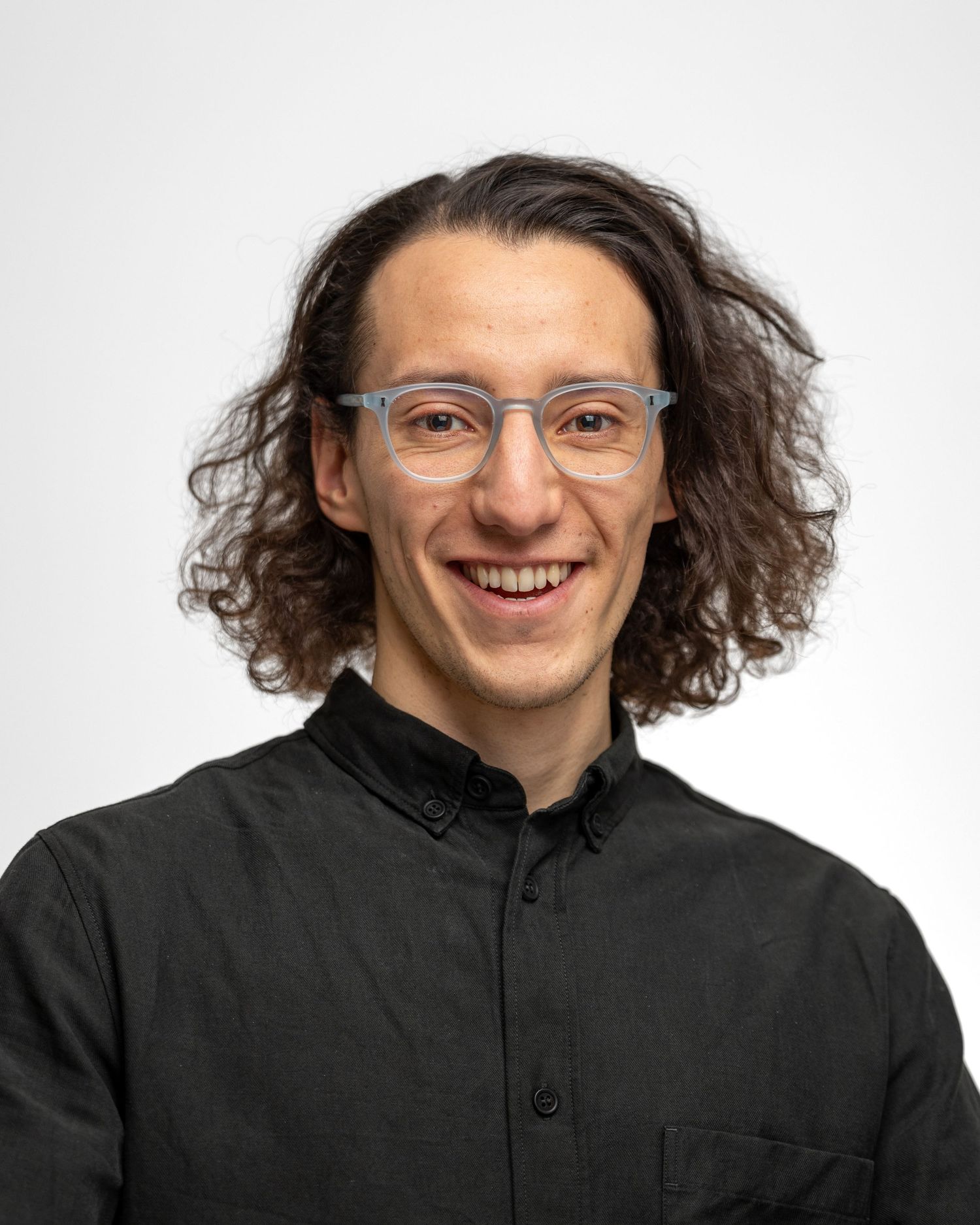 Portrait of someone with curly hair wearing glasses and black top against white background.