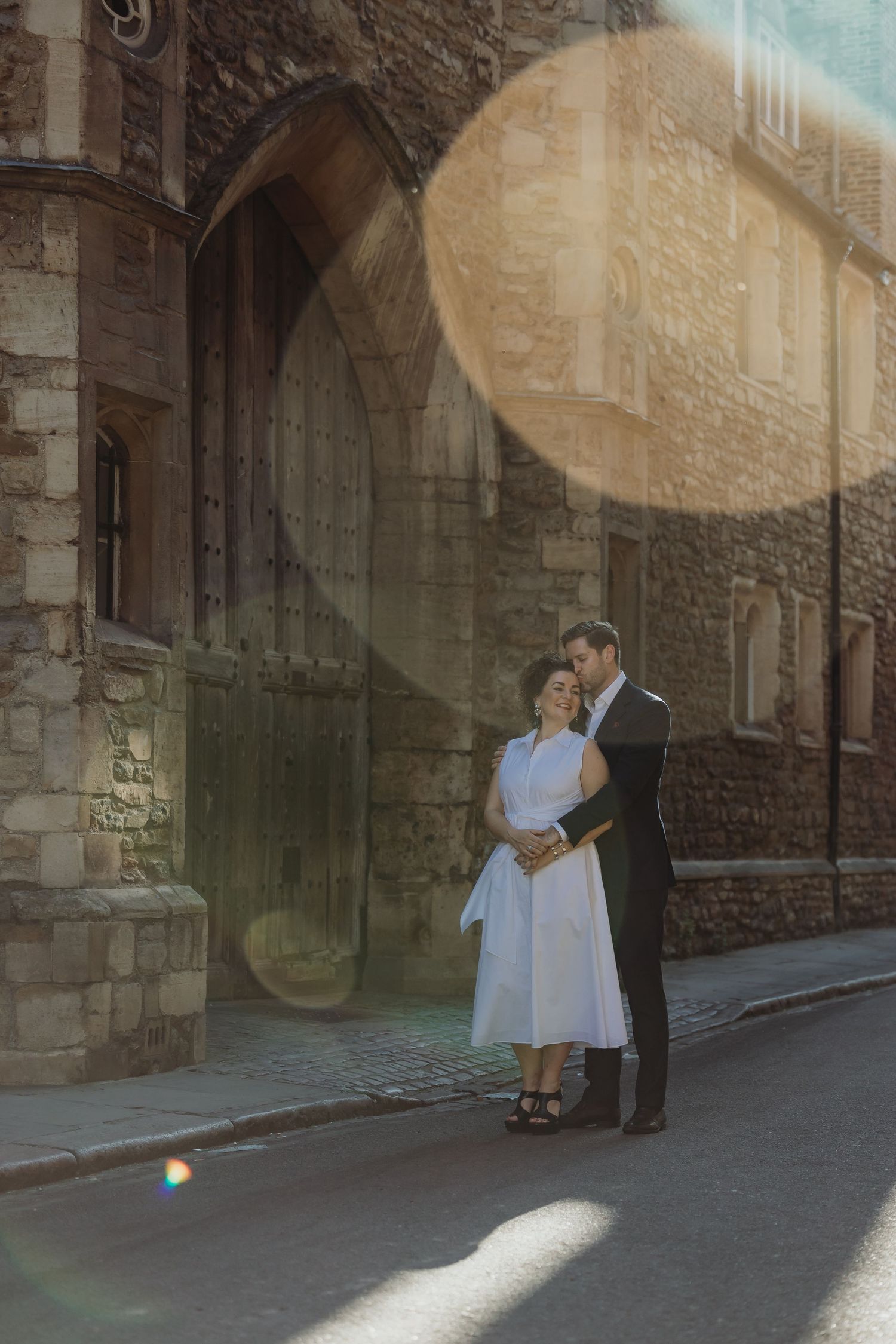 Couple standing in sunlit stone archway during romantic photoshoot.