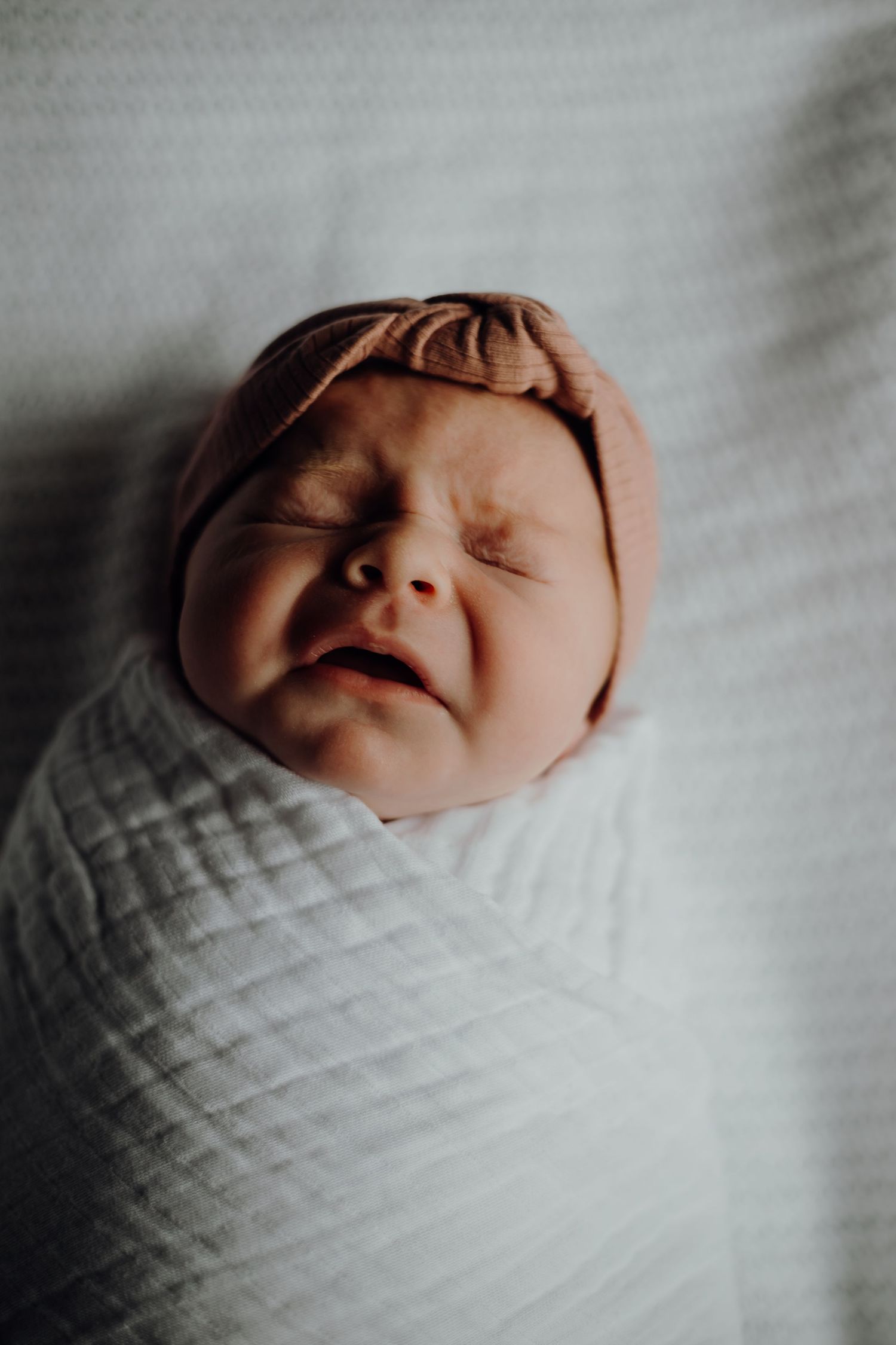 Sleeping newborn wrapped in white textured blanket with peaceful expression.