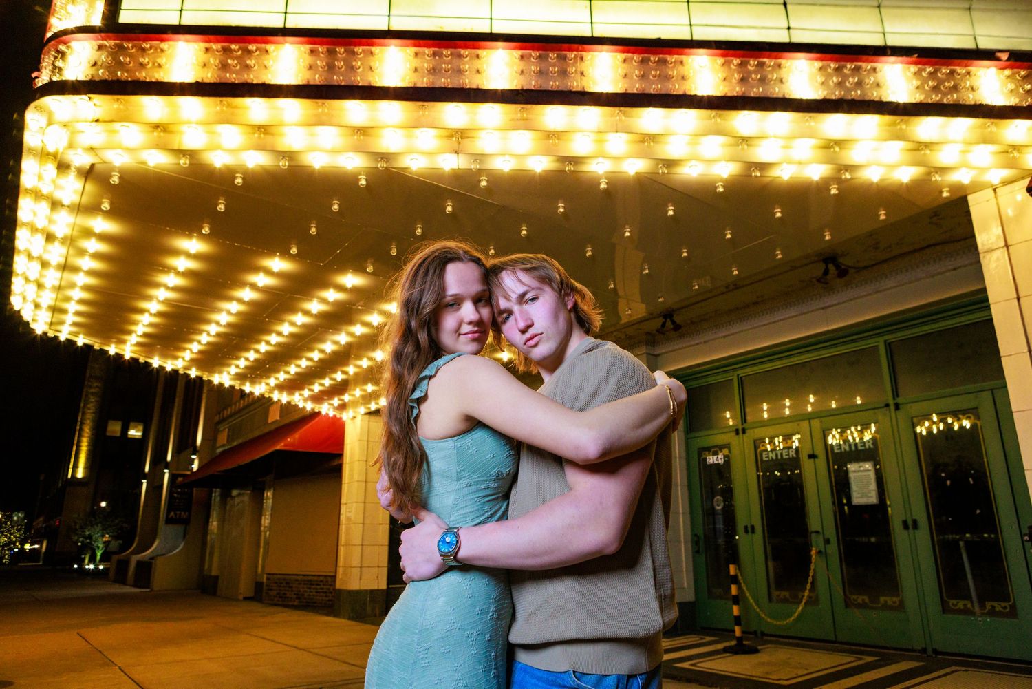 Couple embracing romantically under glowing theater marquee lights at night outside a vintage cinema.