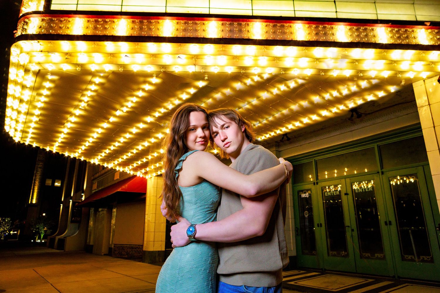 Couple embracing romantically under glowing marquee lights outside a theater at night.