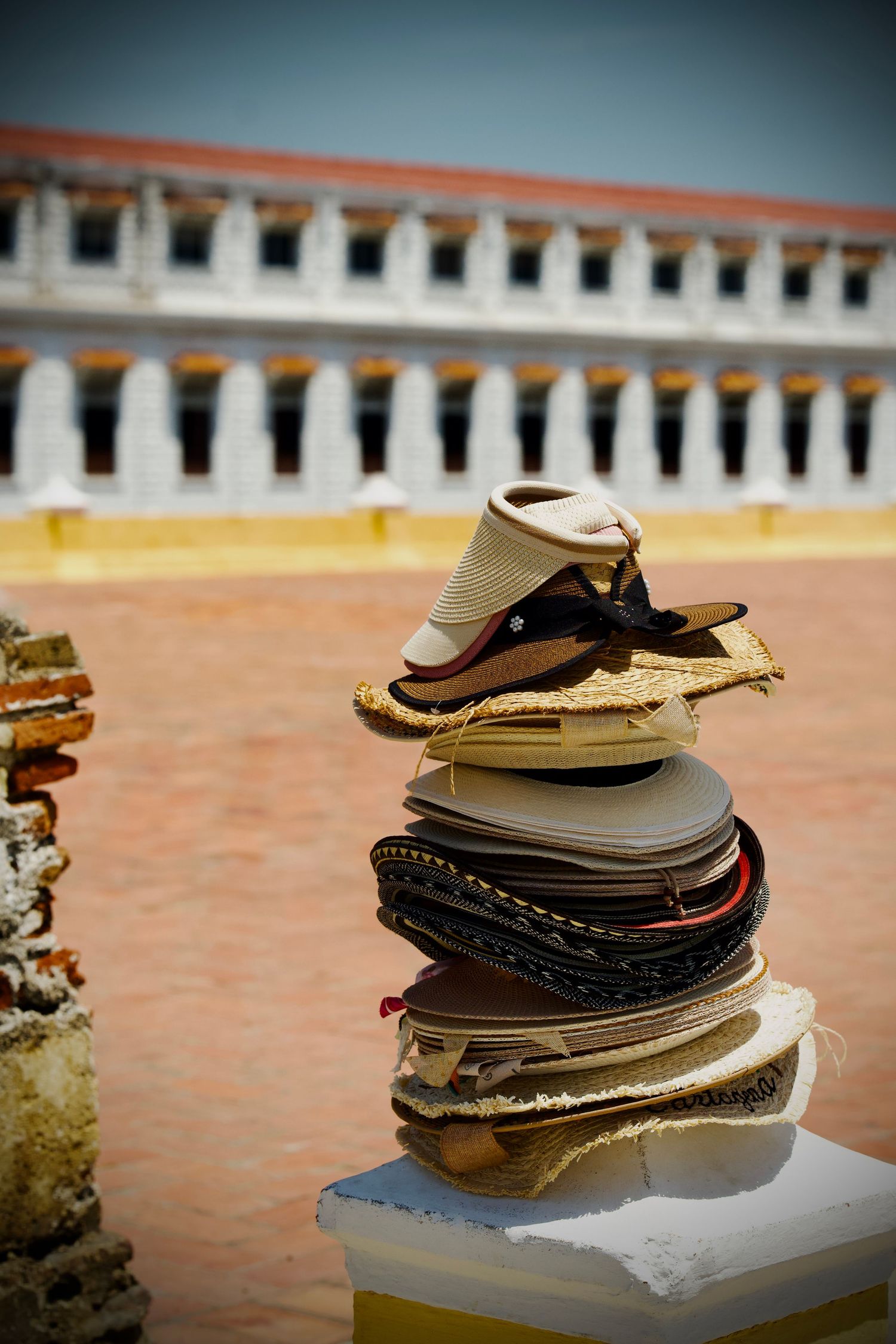 Stack of worn leather shoes and sandals on a white surface against an orange wall.