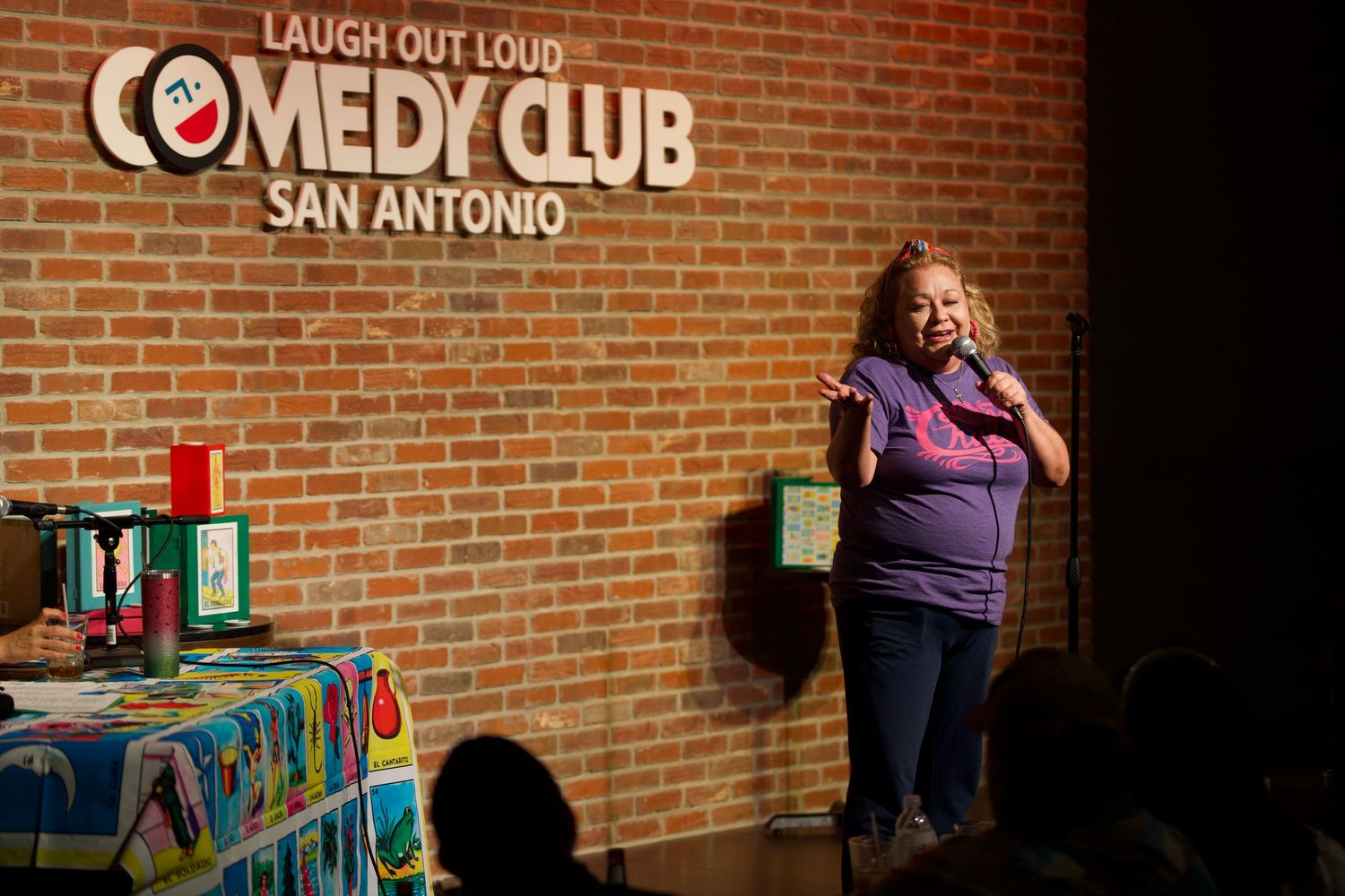Comedy club stage setup with brick wall backdrop and 'Laugh Out Loud' branding visible.