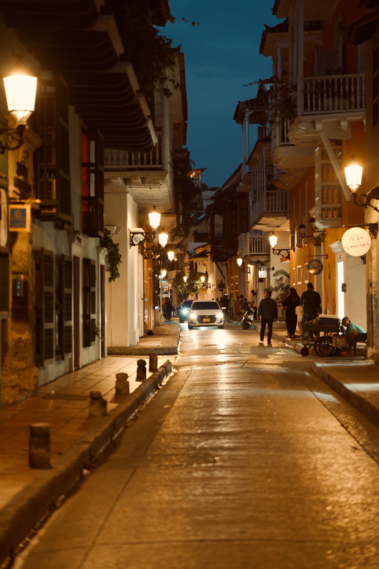Cobblestone street lit by vintage lampposts at night in colonial town.