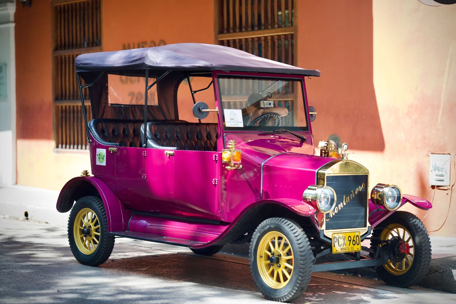 Vintage pink classic cars parked in front of a colonial building with orange walls.