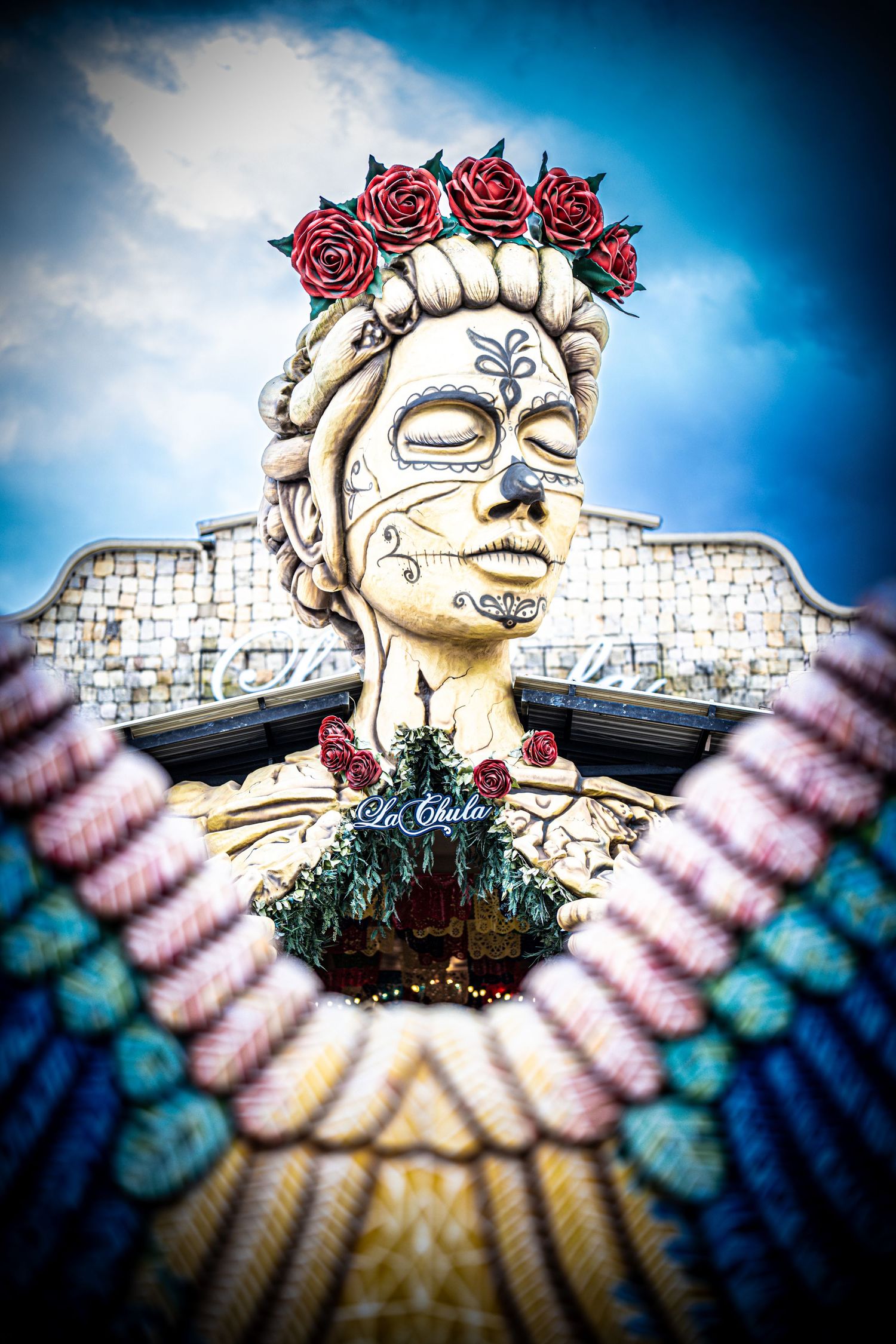 Artistic sculpture of a winged figure with roses against bright blue sky.