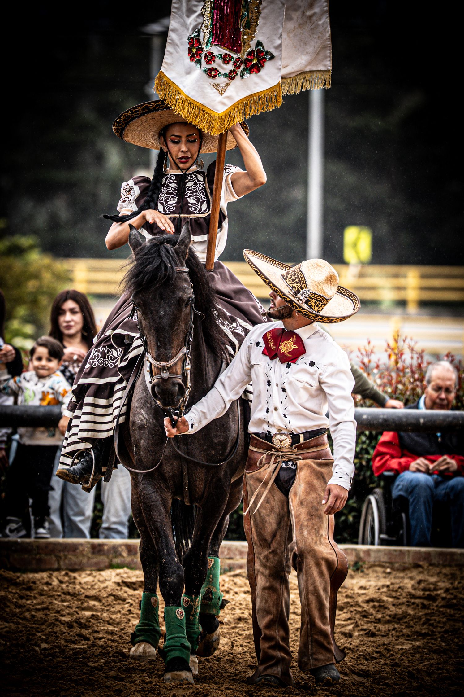 Charros perform traditional Mexican equestrian skills in a dirt arena with spectators watching.
