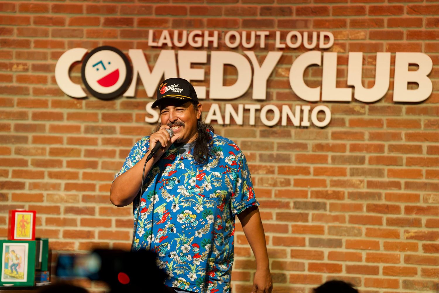 Performer in tropical print shirt entertaining audience at San Antonio Comedy Club.