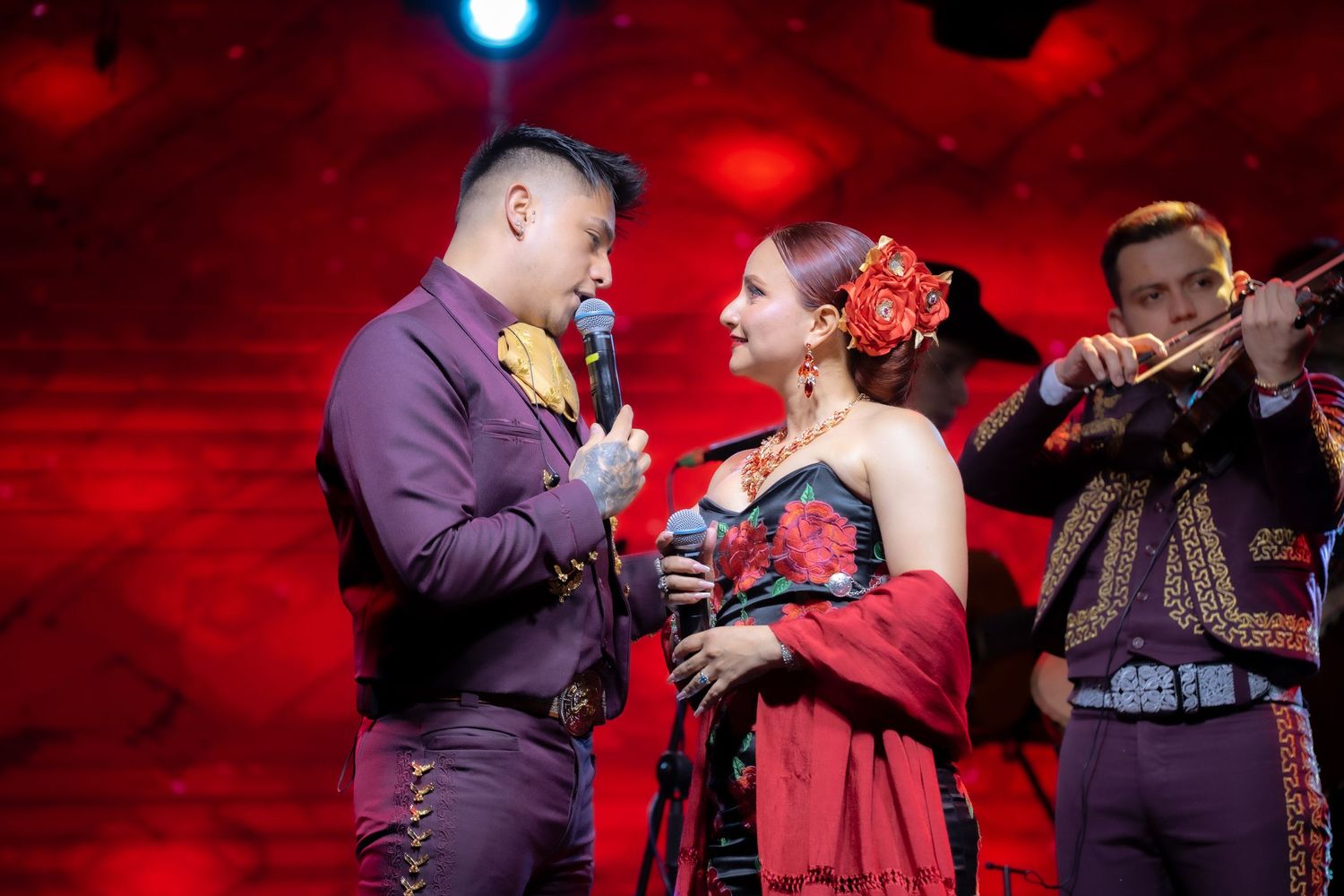 Musicians performing on stage with dramatic red lighting and traditional mariachi costumes.