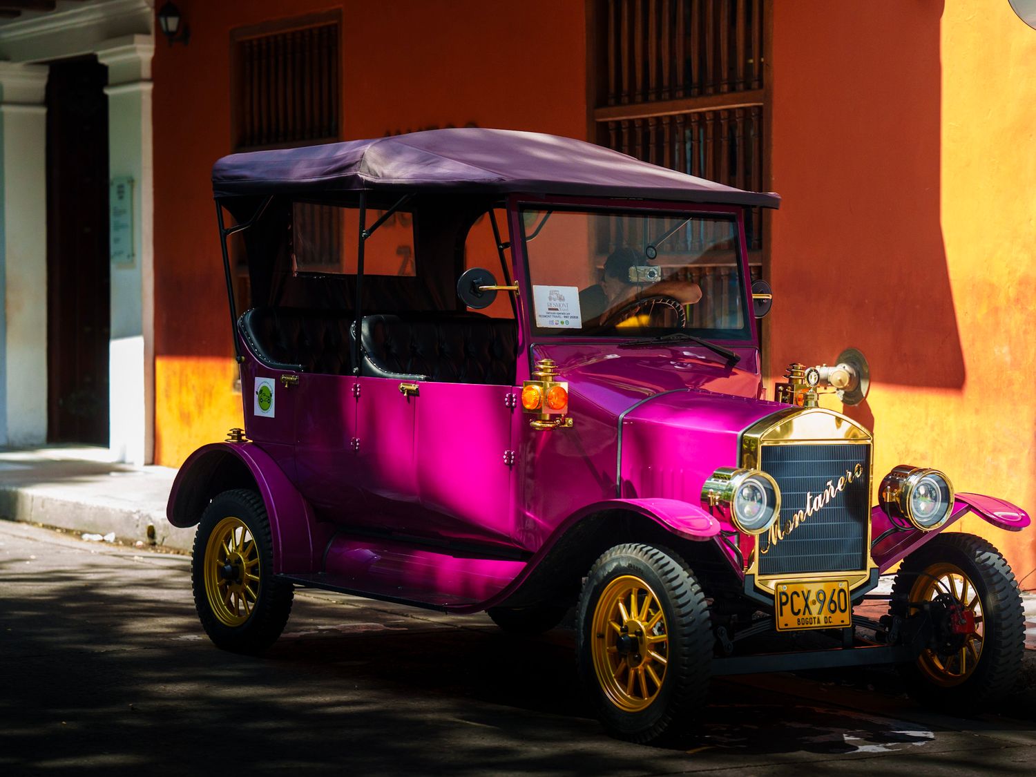 Bright pink vintage cars lined up against colorful colonial buildings.