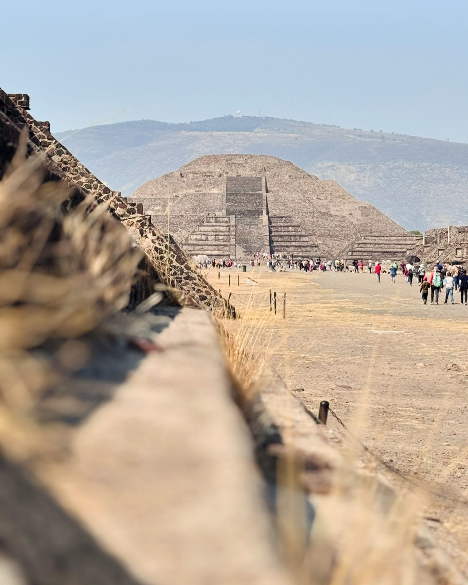 Ancient Aztec pyramids and ruins with tourists walking along desert landscape.