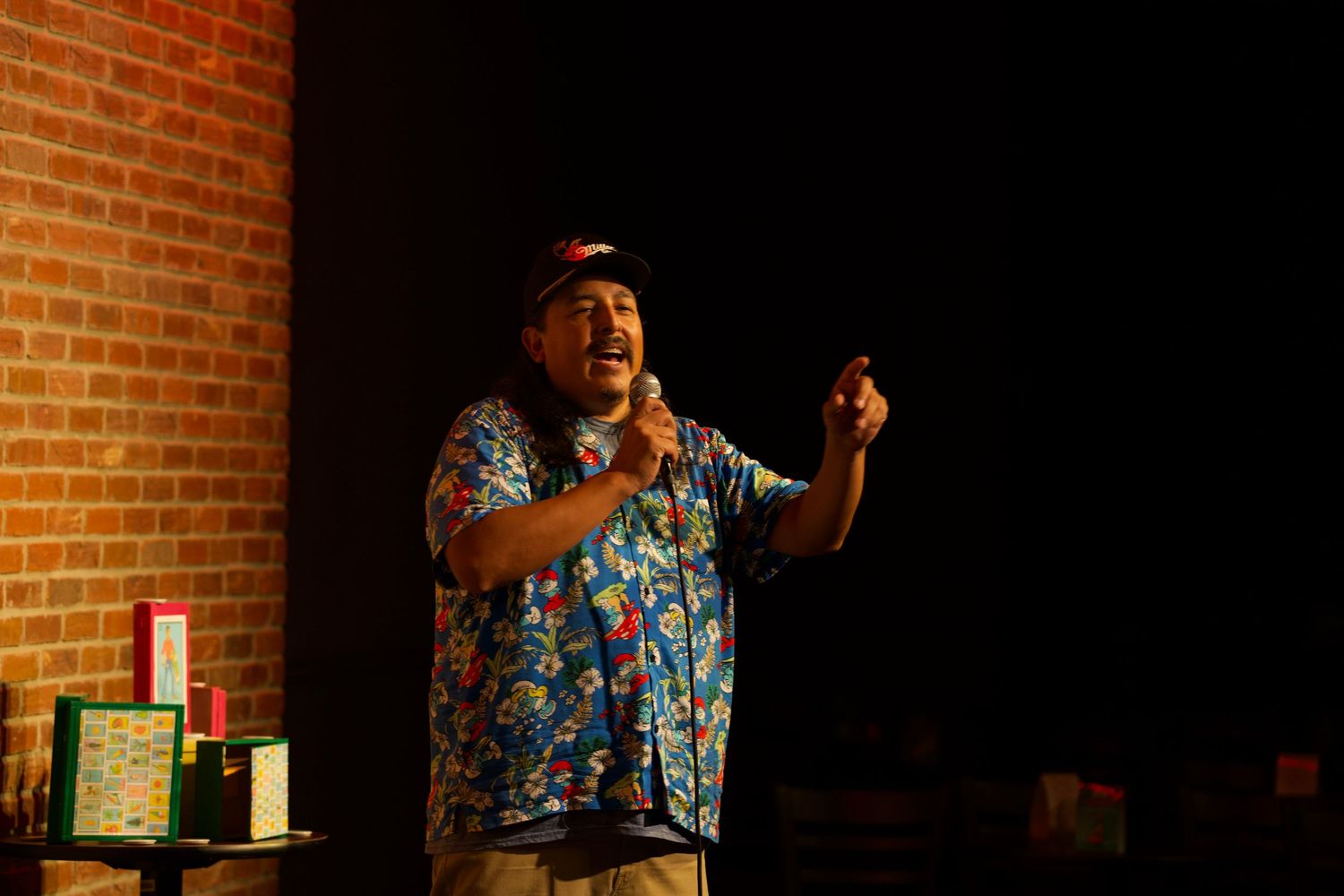 Stand-up comedian in floral shirt performing at comedy club stage.