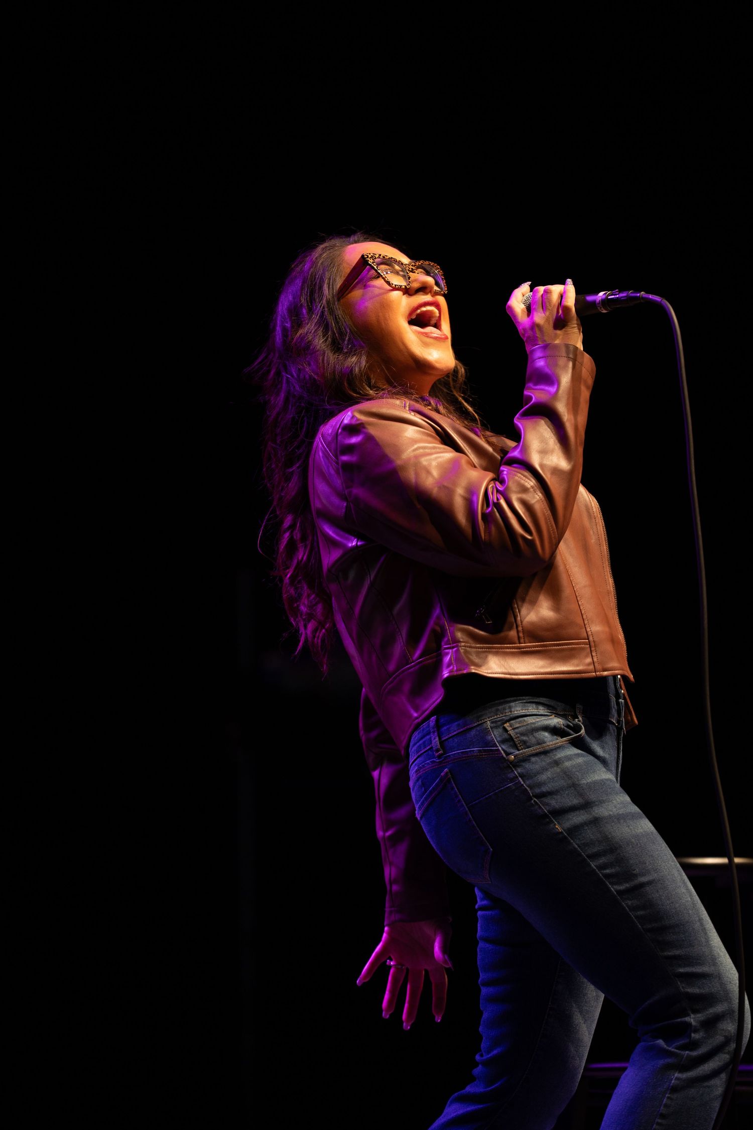 Dramatic silhouette of a performer singing passionately on stage under purple lighting.