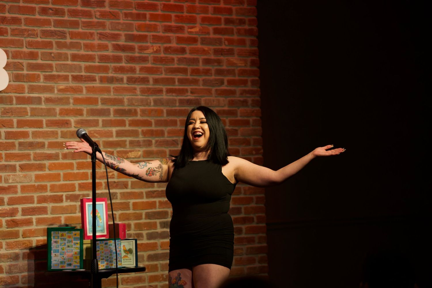 Comedian gestures expressively during performance at brick-walled comedy venue.