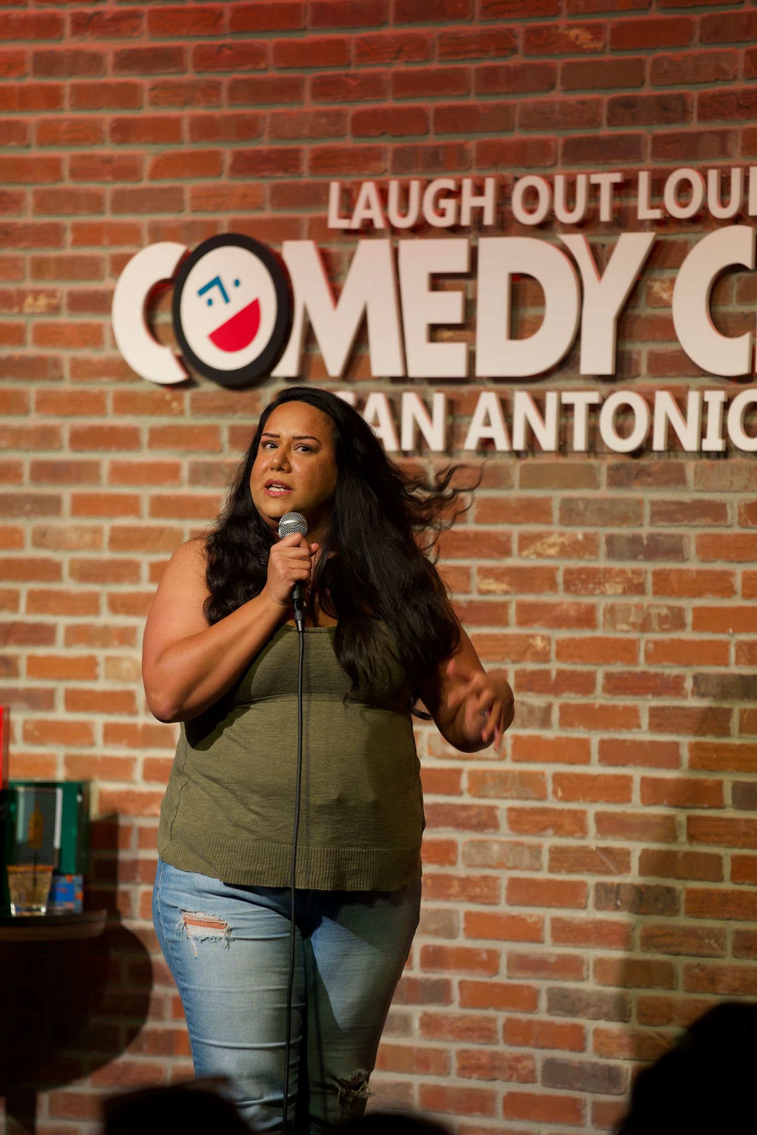 Comedian performing on stage at Laugh Out Loud Comedy Club with brick wall backdrop.
