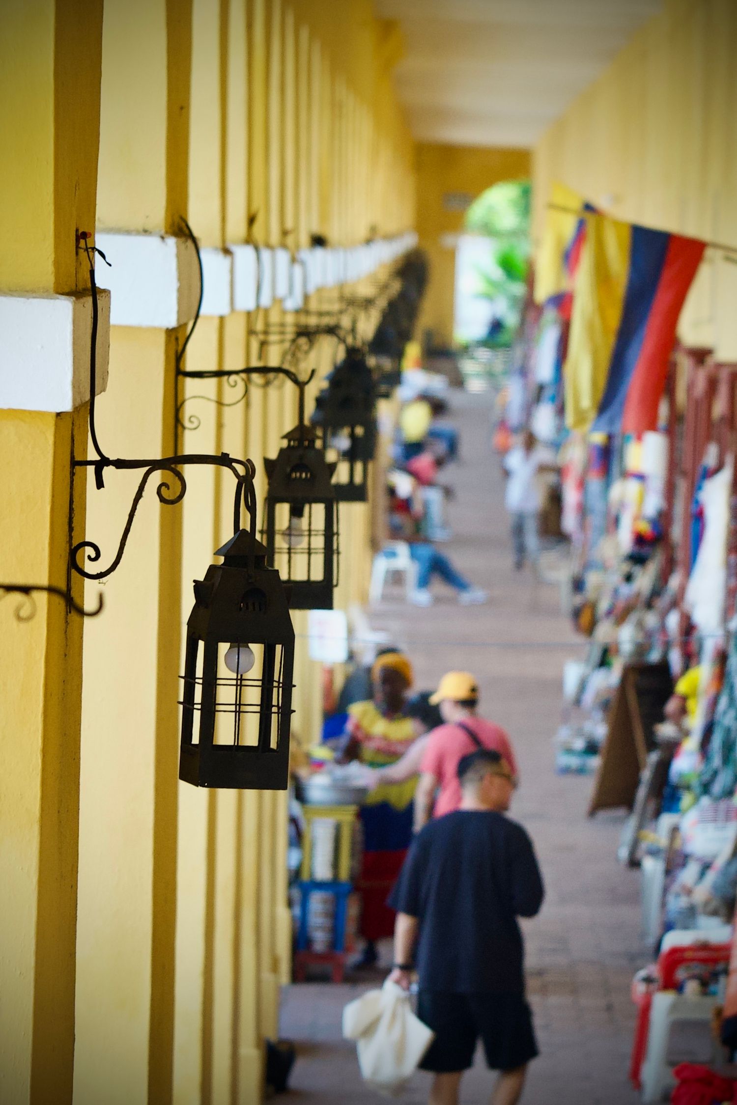 Yellow colonnade corridor with hanging textiles and market stalls in the distance.