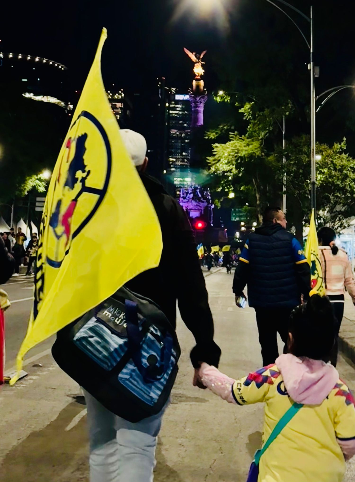 Nighttime street scene with person carrying yellow flag among city lights.