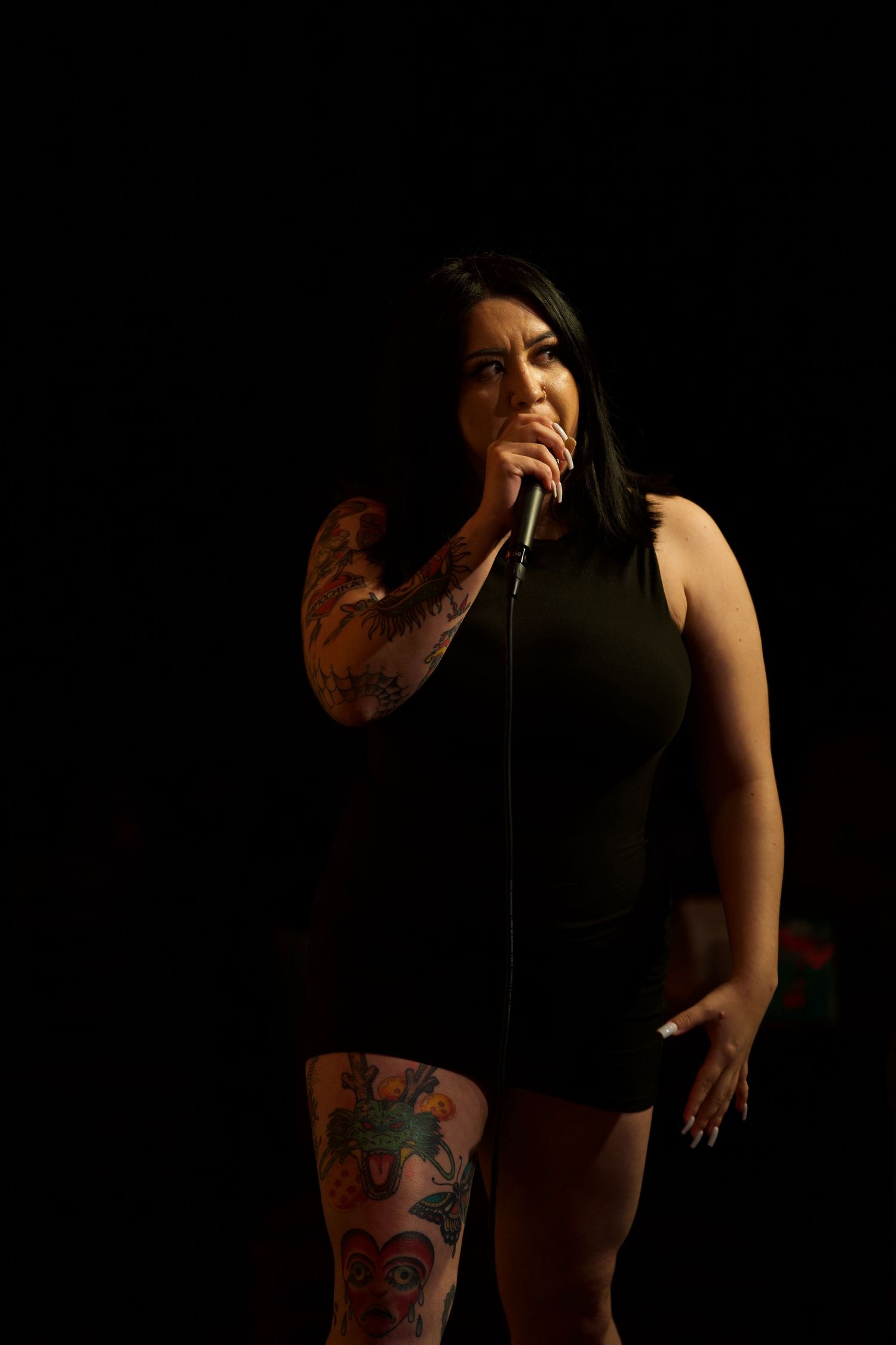 Performer in black outfit on dark stage with dramatic lighting at comedy club.