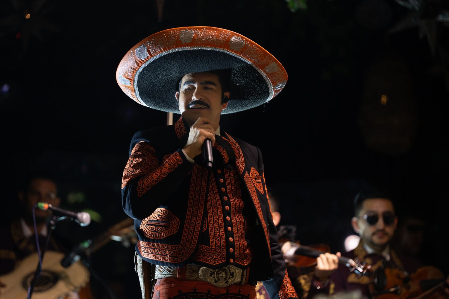Mariachi singer performing on dark stage wearing traditional sombrero and embroidered outfit.