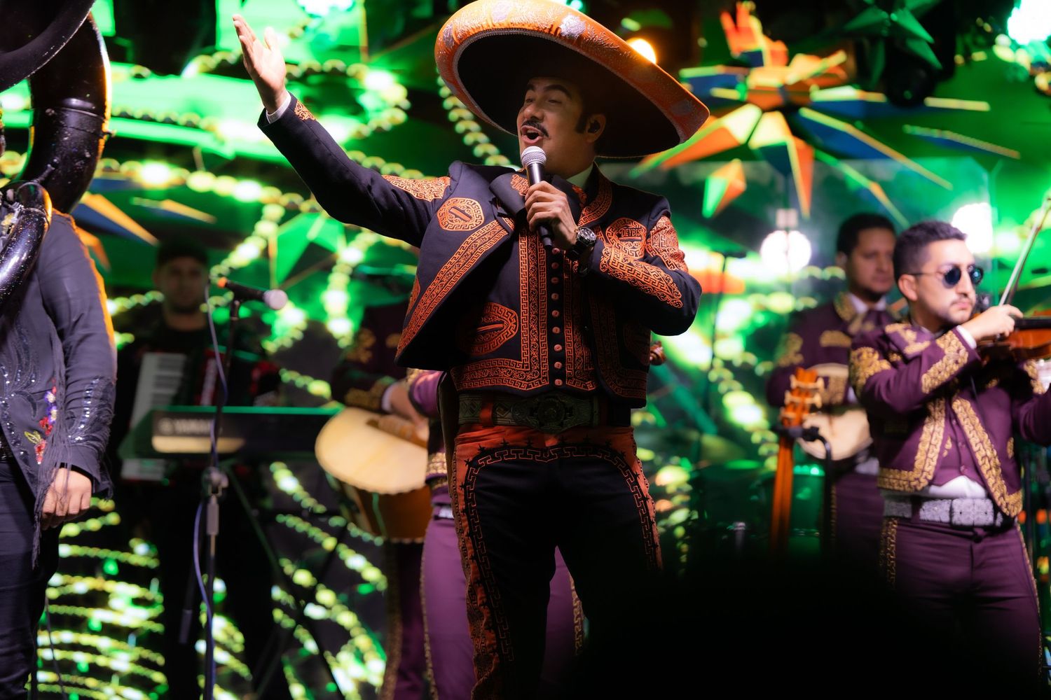 Musicians perform traditional Mexican music with colorful green stage lighting.