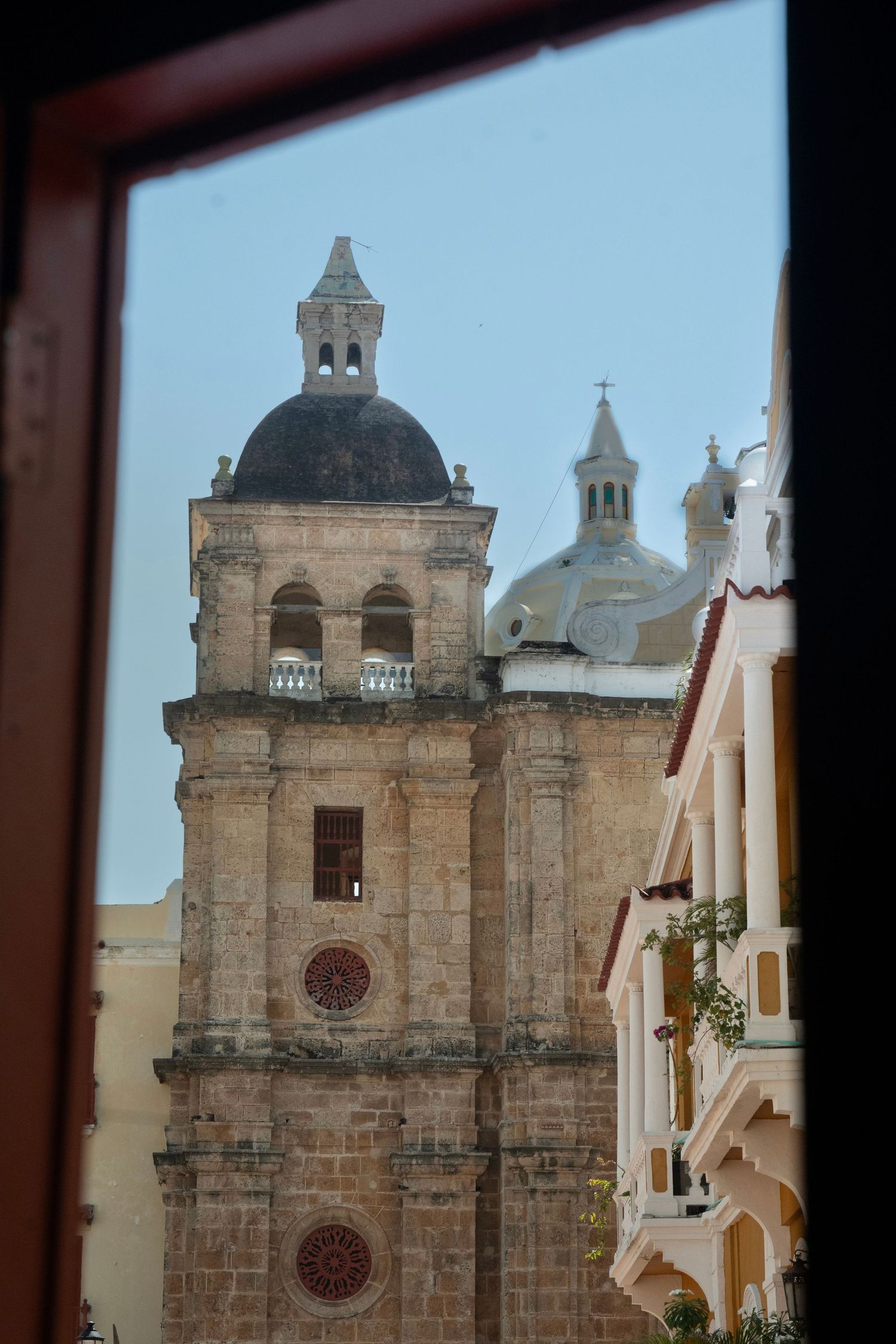 Stone church towers and domes viewed through a window frame against blue sky.