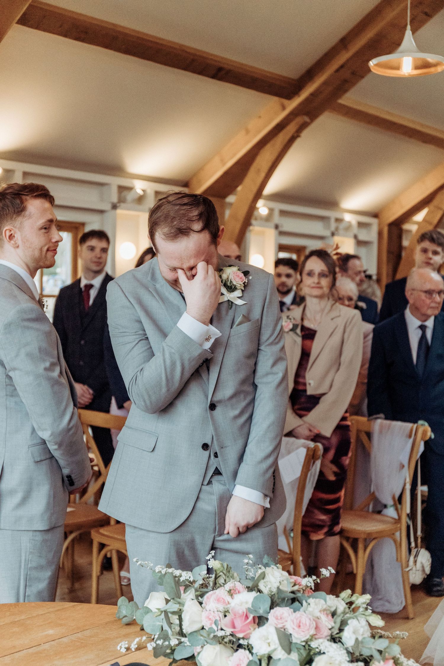 A groom wipes away emotion during the ceremony as guests look on, capturing a heartfelt moment.