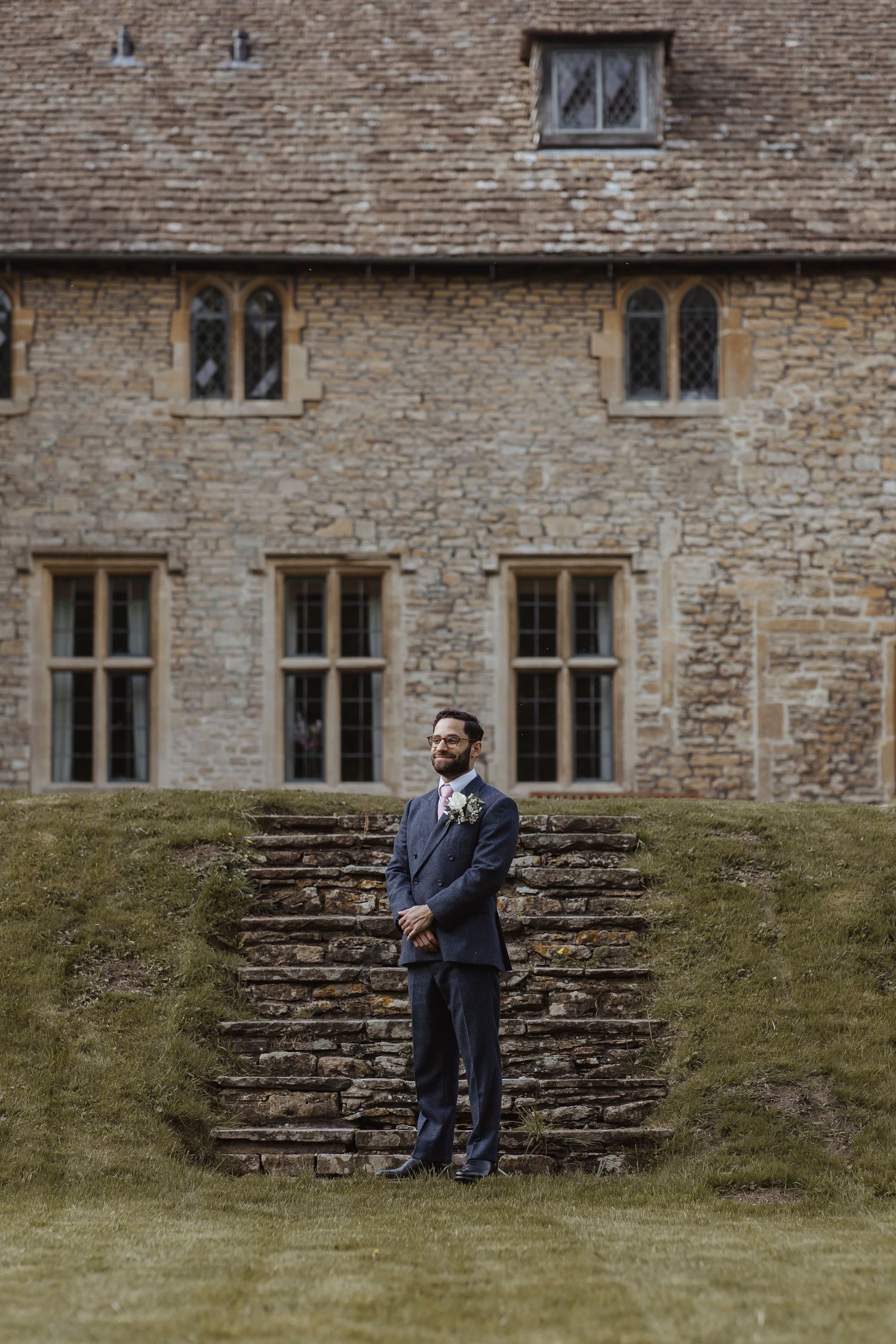 groom standing proudly at the bottom of steps in front of a country house