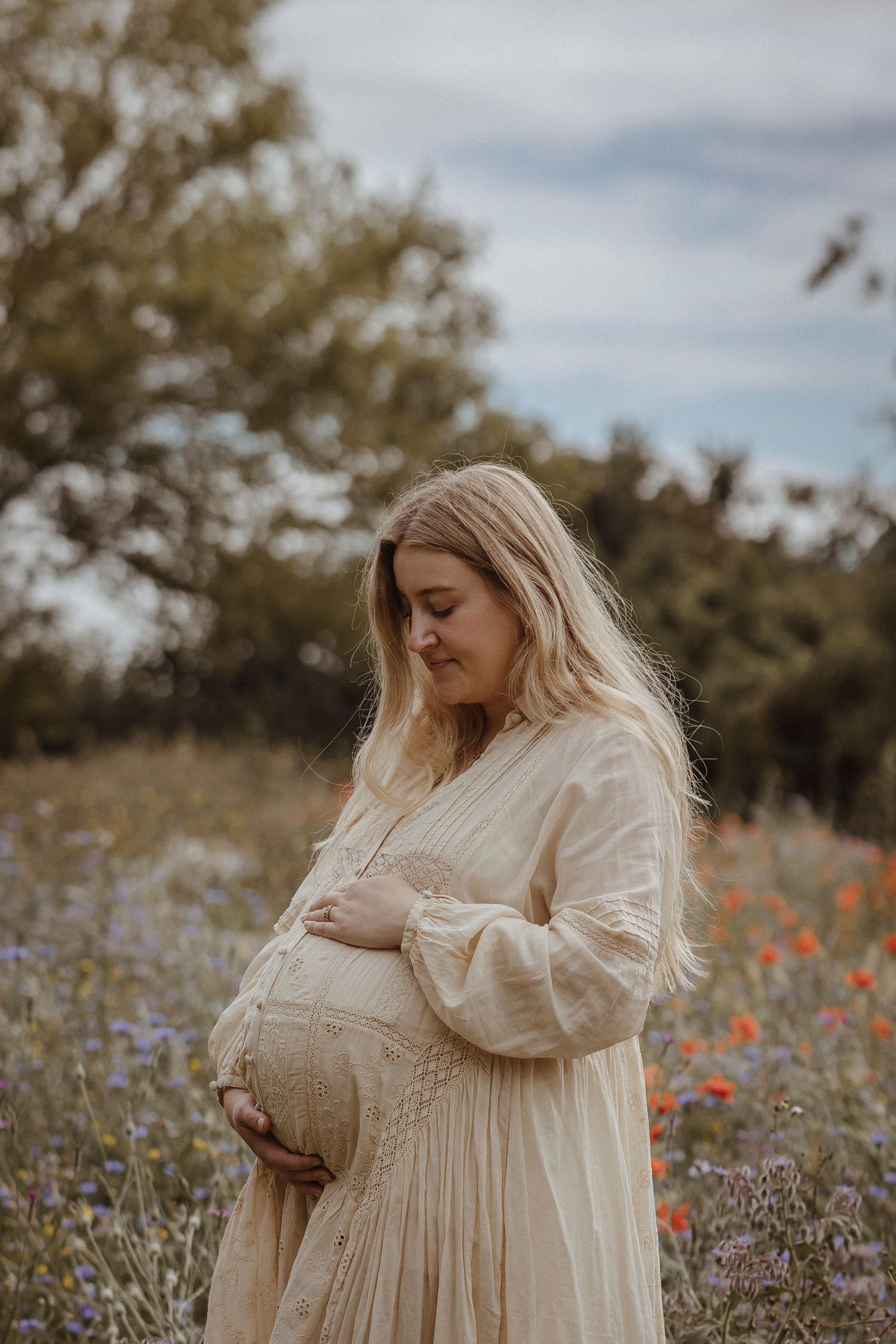 mother holding her bump in a field of wild flowers with a blue sky behind