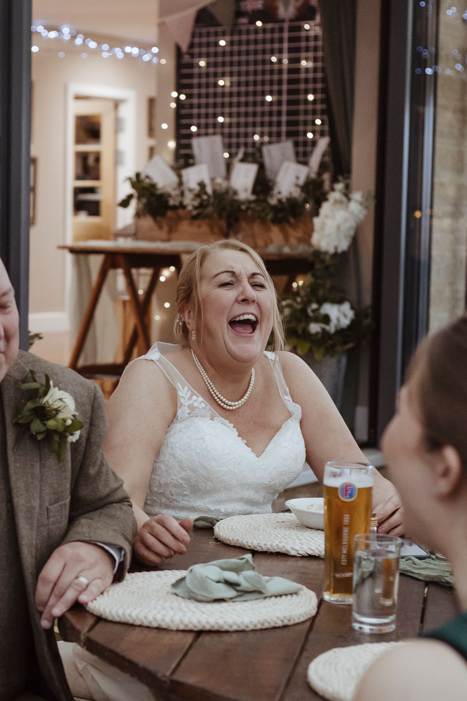 She shares a big, joyful laugh at the table, radiating happiness in her wedding dress.