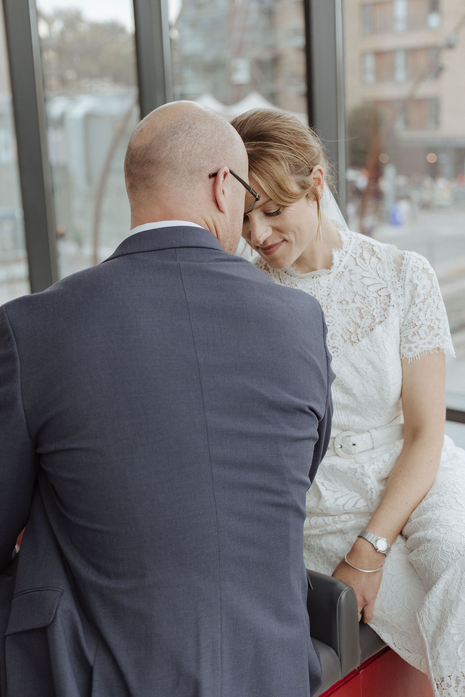 bride and groom touching foreheads whilst sat down with views through the window behind them