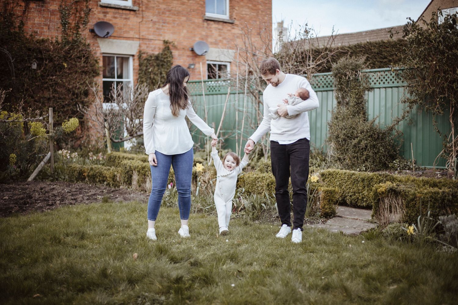 mother and father holding daughters hands whilst walking in the garden