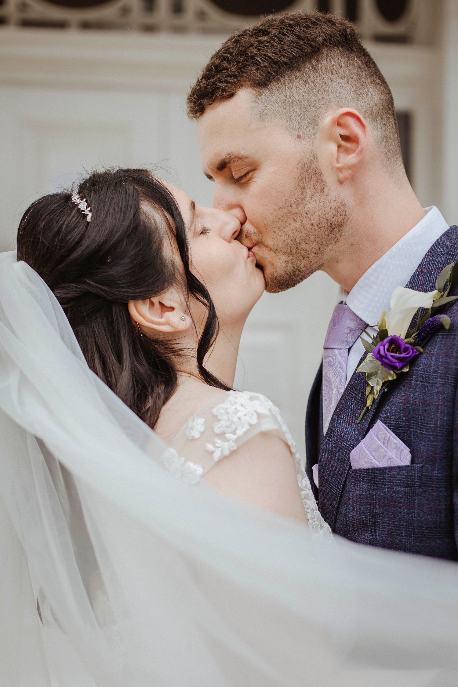 A bride and groom share a close, tender kiss, her veil flowing as they embrace.