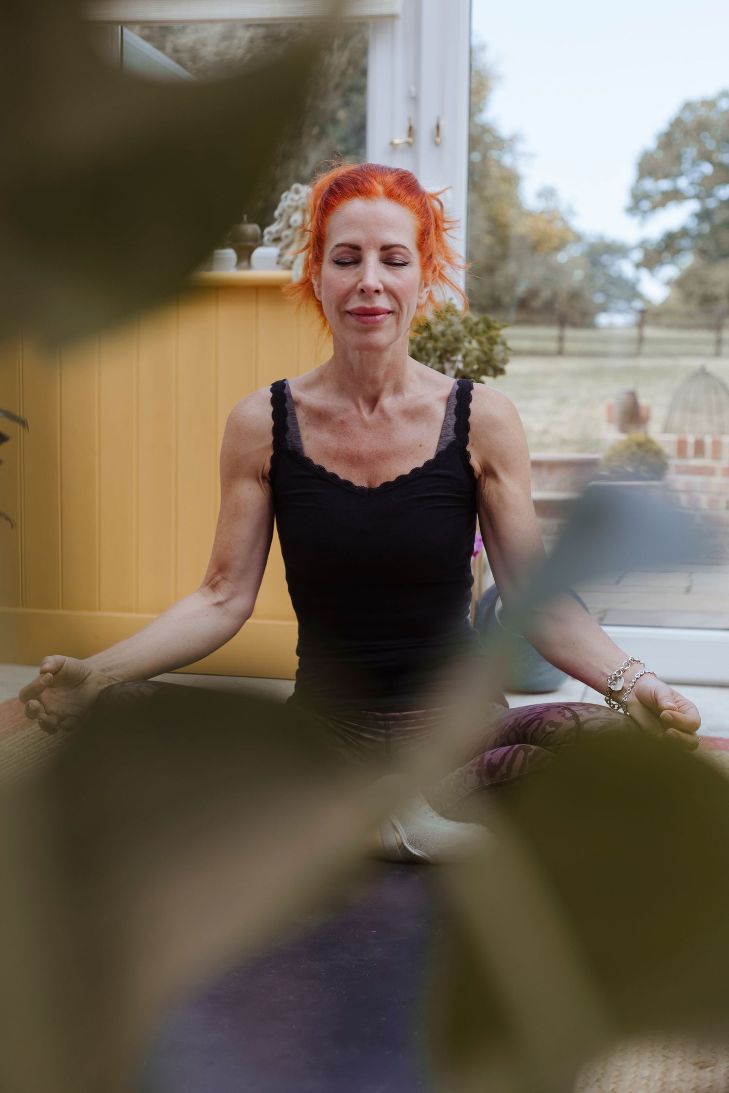 A woman sits cross-legged indoors, eyes closed, calmly meditating.
