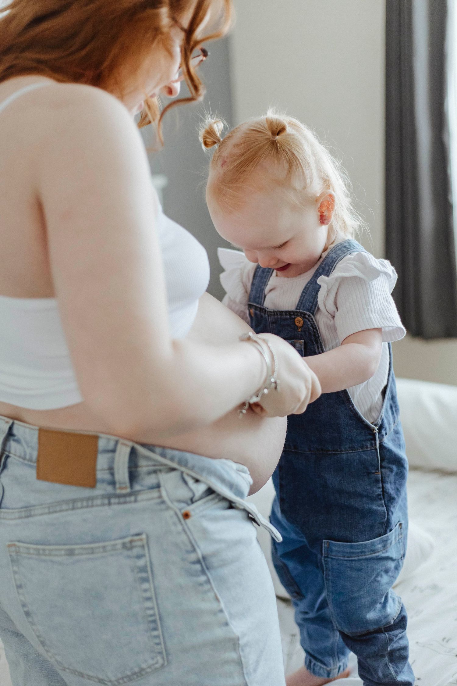 A toddler curiously touches a pregnant belly, sharing a sweet, quiet moment with their parent.