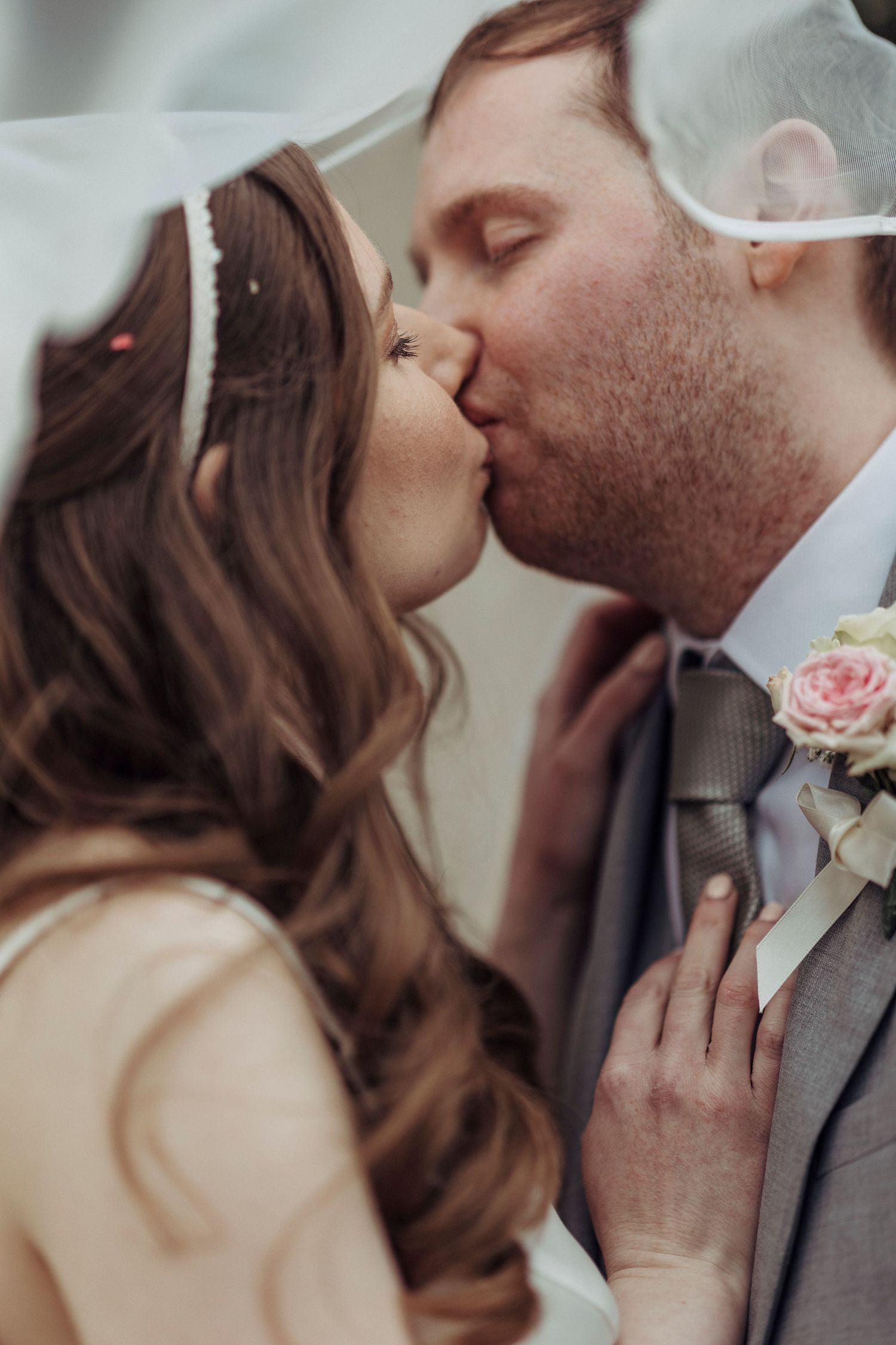 A newlywed couple share a soft, romantic kiss beneath a flowing veil.