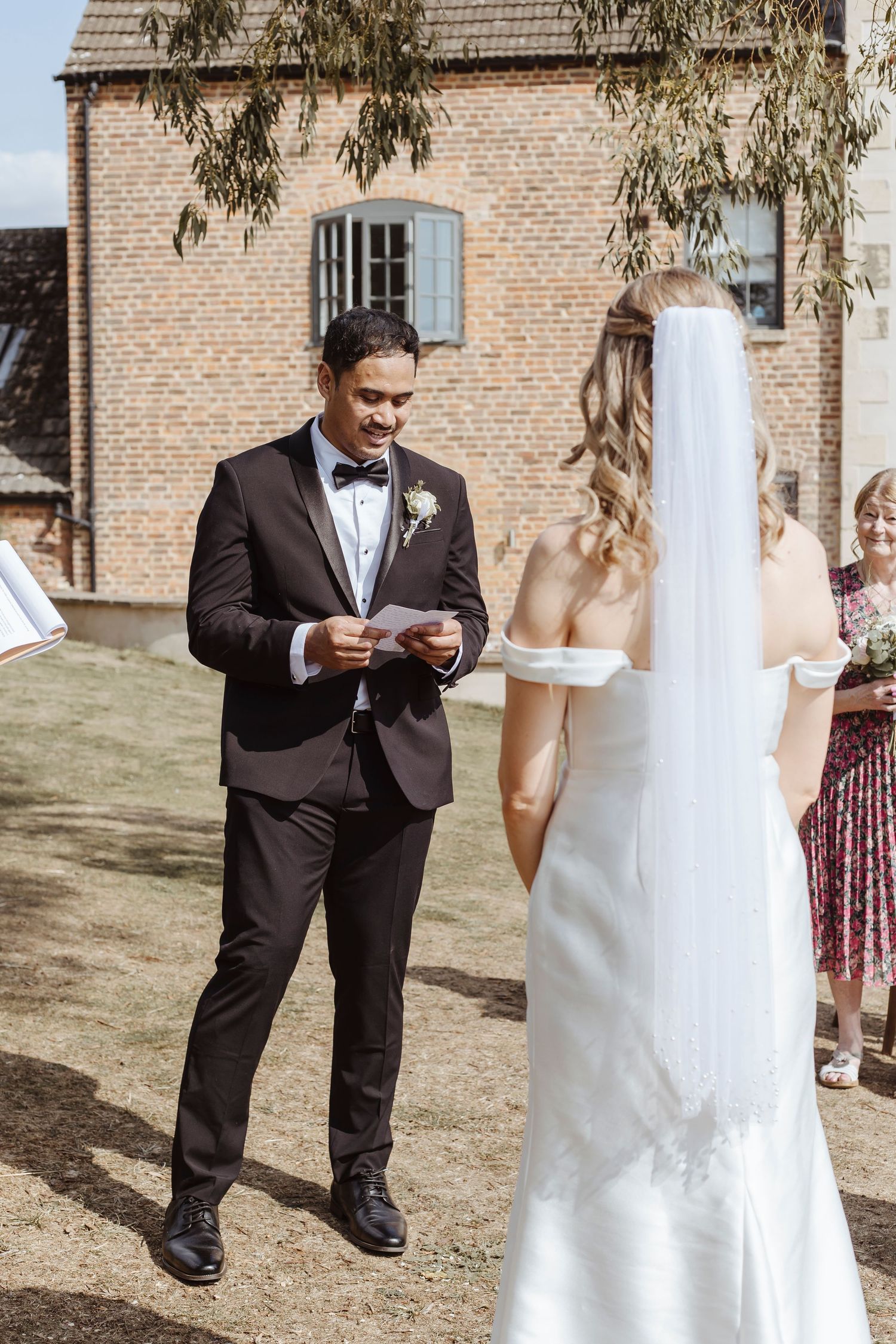 groom reading out his vows on a sunny day whilst his bride listens