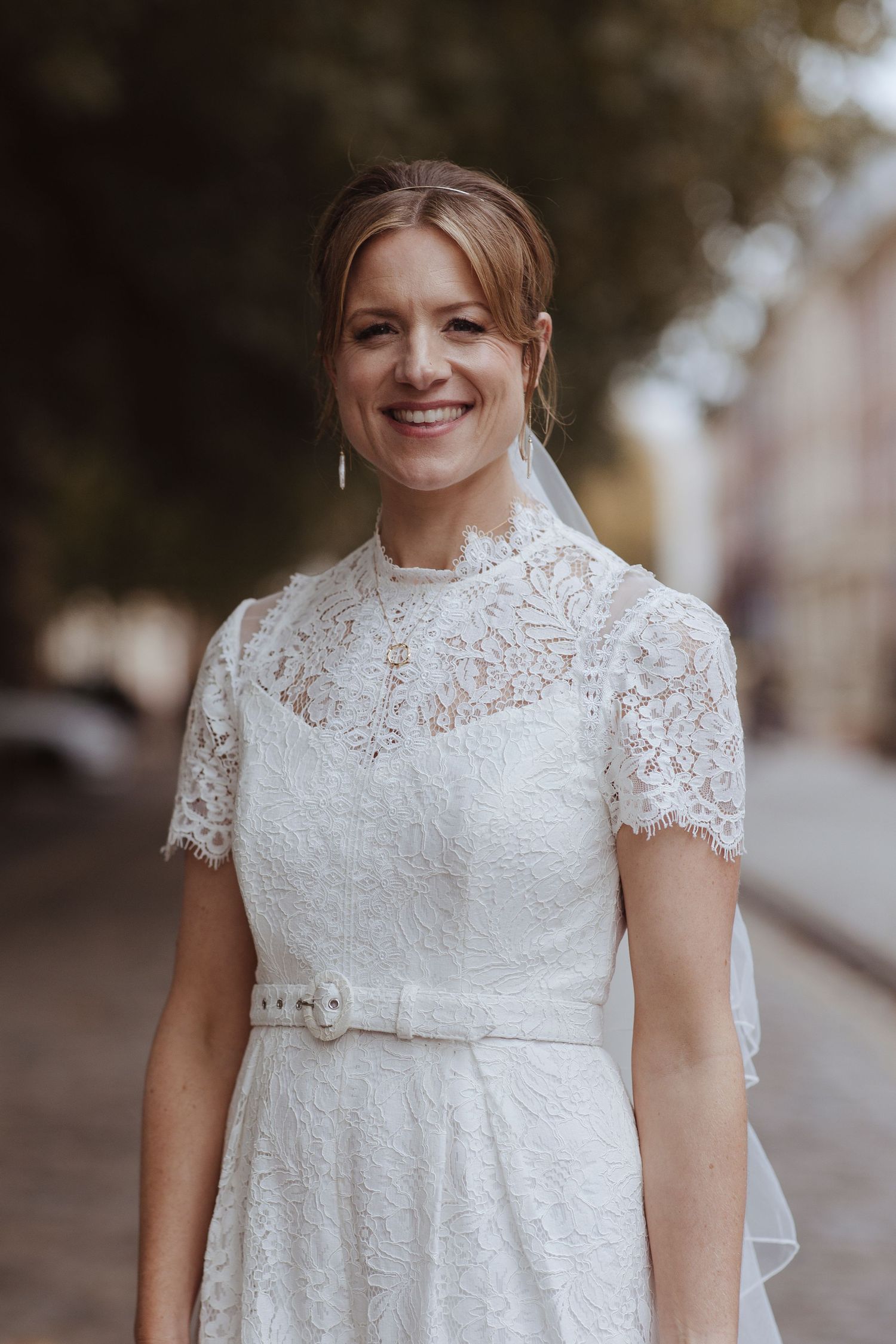 bride portrait- standing on a cable street smiling with green trees behind her