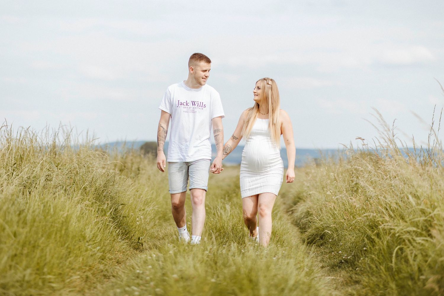A couple walks hand in hand through a tall grassy path, sharing a warm, happy moment together.