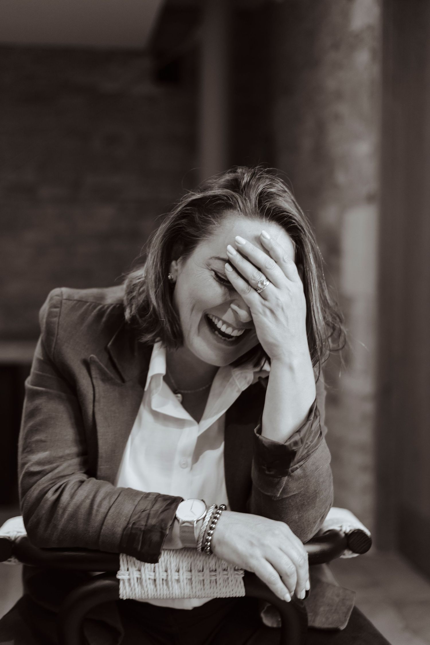 A woman laughs wholeheartedly, covering part of her face with her hand in a candid, joyful moment.
