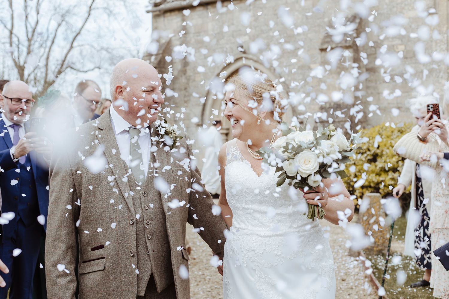 The couple walks through a joyful shower of confetti, smiling at each other as loved ones celebrate around them.